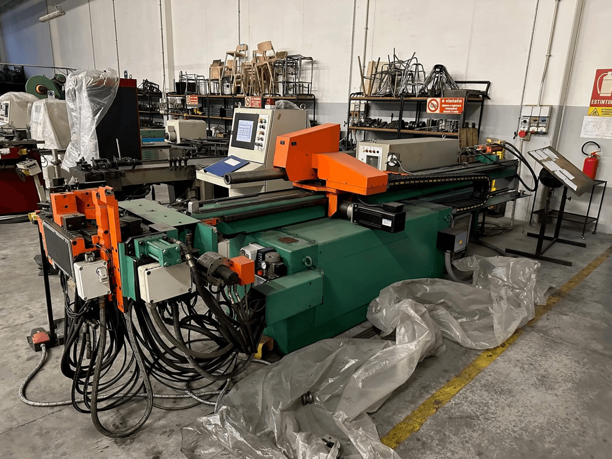 Ipari gép narancssárga és zöld színű karosszériával, vezérlőpanellel és számos kábellel, szemből nézve, műhelyben.