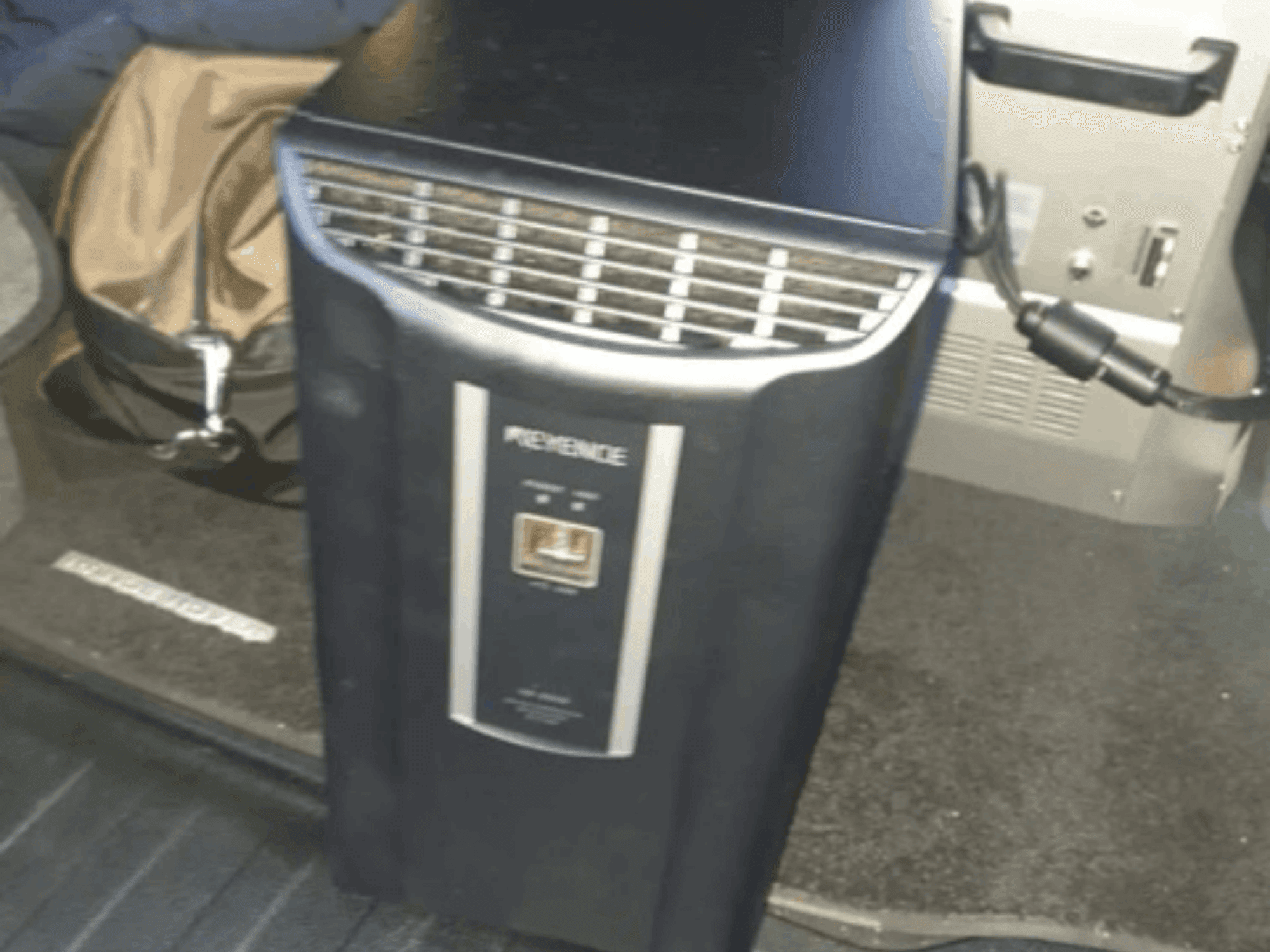 A KEYENCE IM-8030 automatizálási rendszer elölnézetben, a vezérlőpanel és a szellőzőnyílások bemutatásával, a jármű belsejének hátterében.