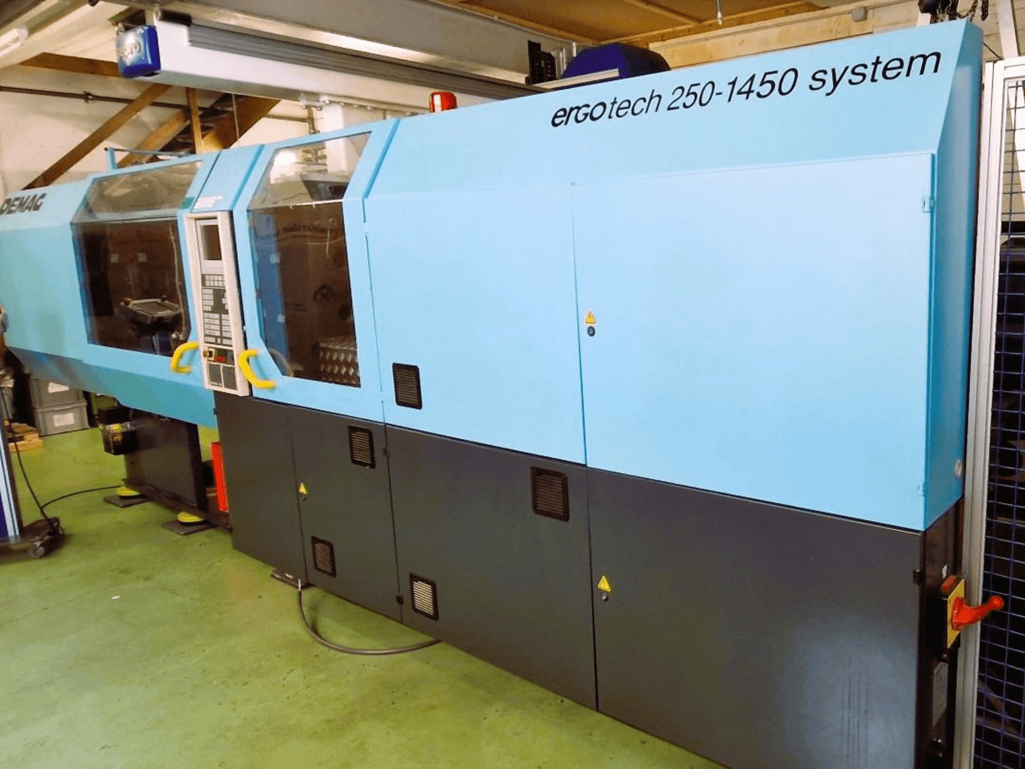 Ergotech 250-1450 rendszerű fröccsöntőgép, elölnézetben, kék és fekete színben, a vezérlőpanel és a biztonsági berendezések láthatóak.