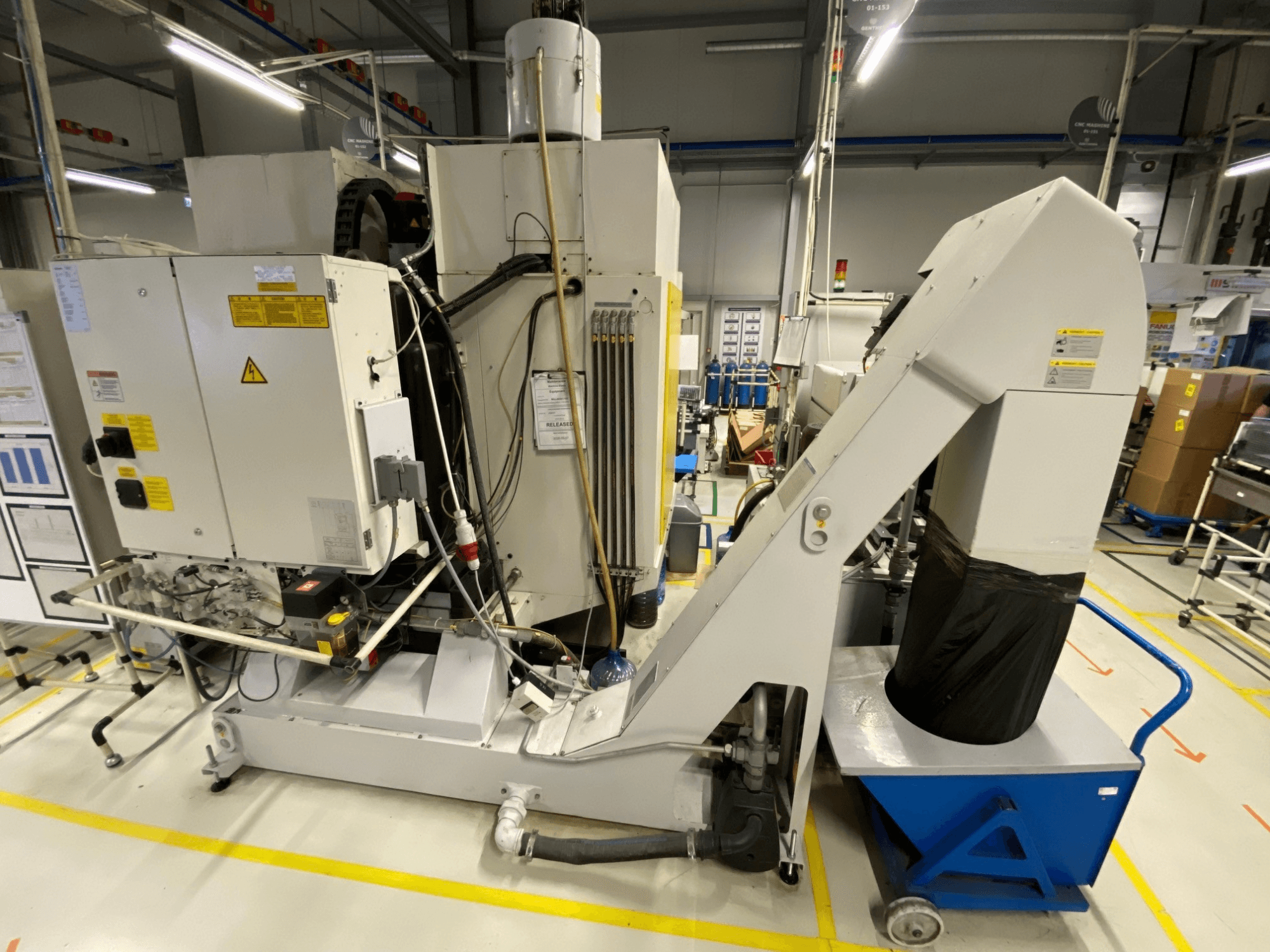 A FANUC ROBODRILL α-D21LiB függőleges megmunkáló központ elölnézete, amelyen láthatók az elektromos alkatrészek és a kivezető csatorna.