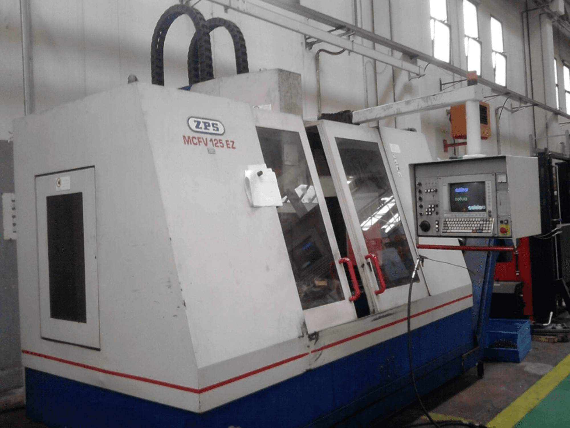 ZPS MCFV 125 EZ CNC gép, elölnézetben, vezérlőpanel és piros fogantyúk, műhelyben, látható tömlőkkel.