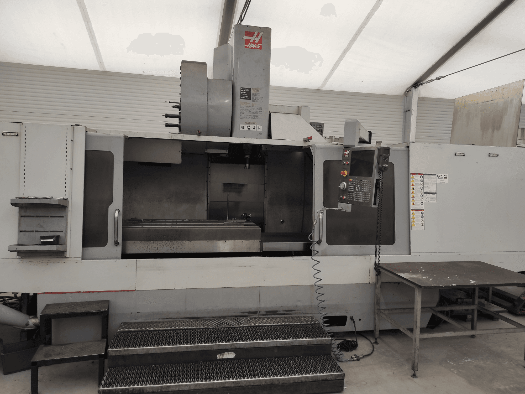 HAAS VF-10/50HE függőleges megmunkálóközpont, elölnézetben a kezelőpanel, a gépágy és a kezelőlépcső.