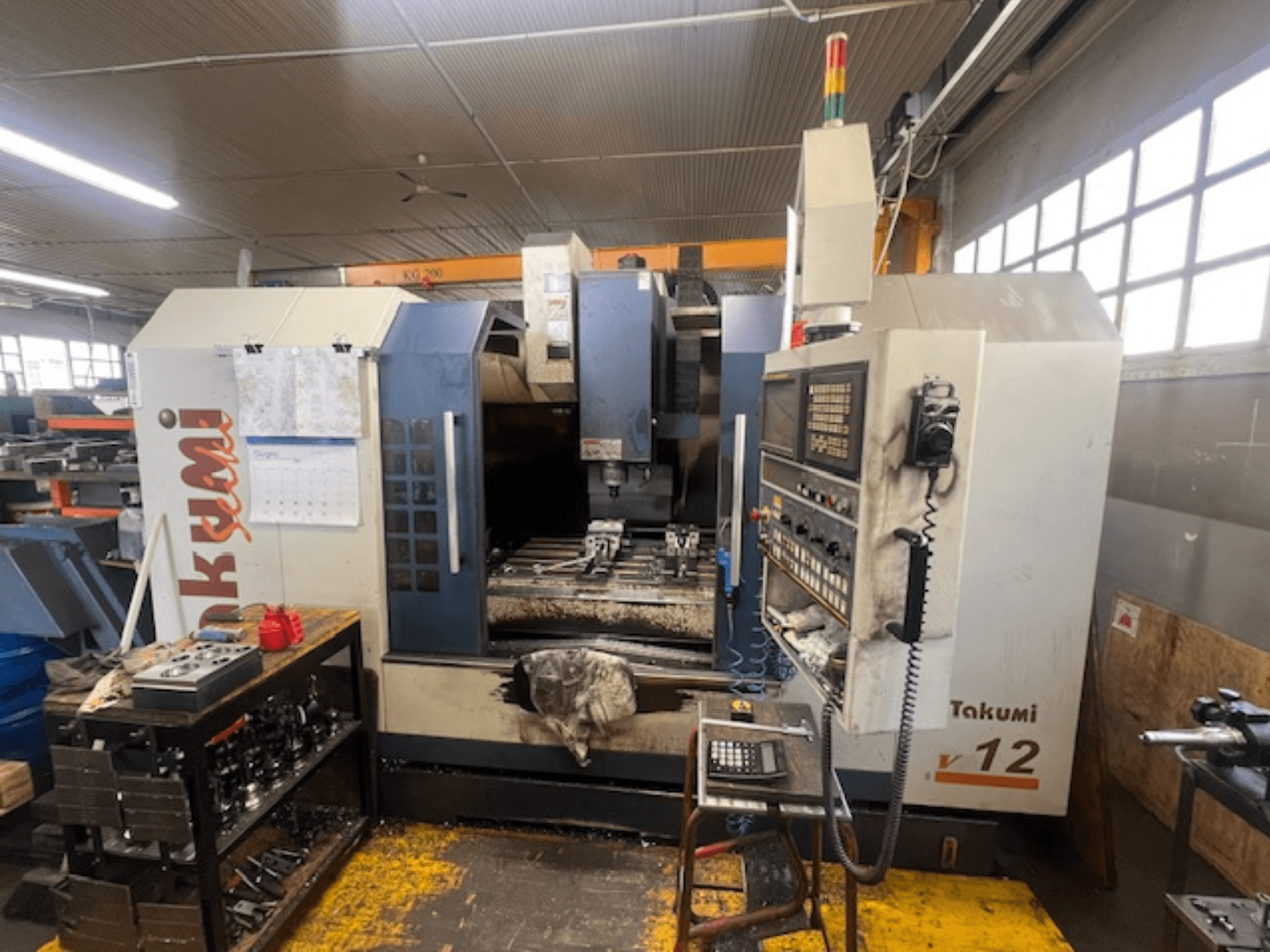 Takumi V12 CNC marógép oldalnézetben, a vezérlőpanel, a vágási terület és a szerszámok a munkaállomáson.