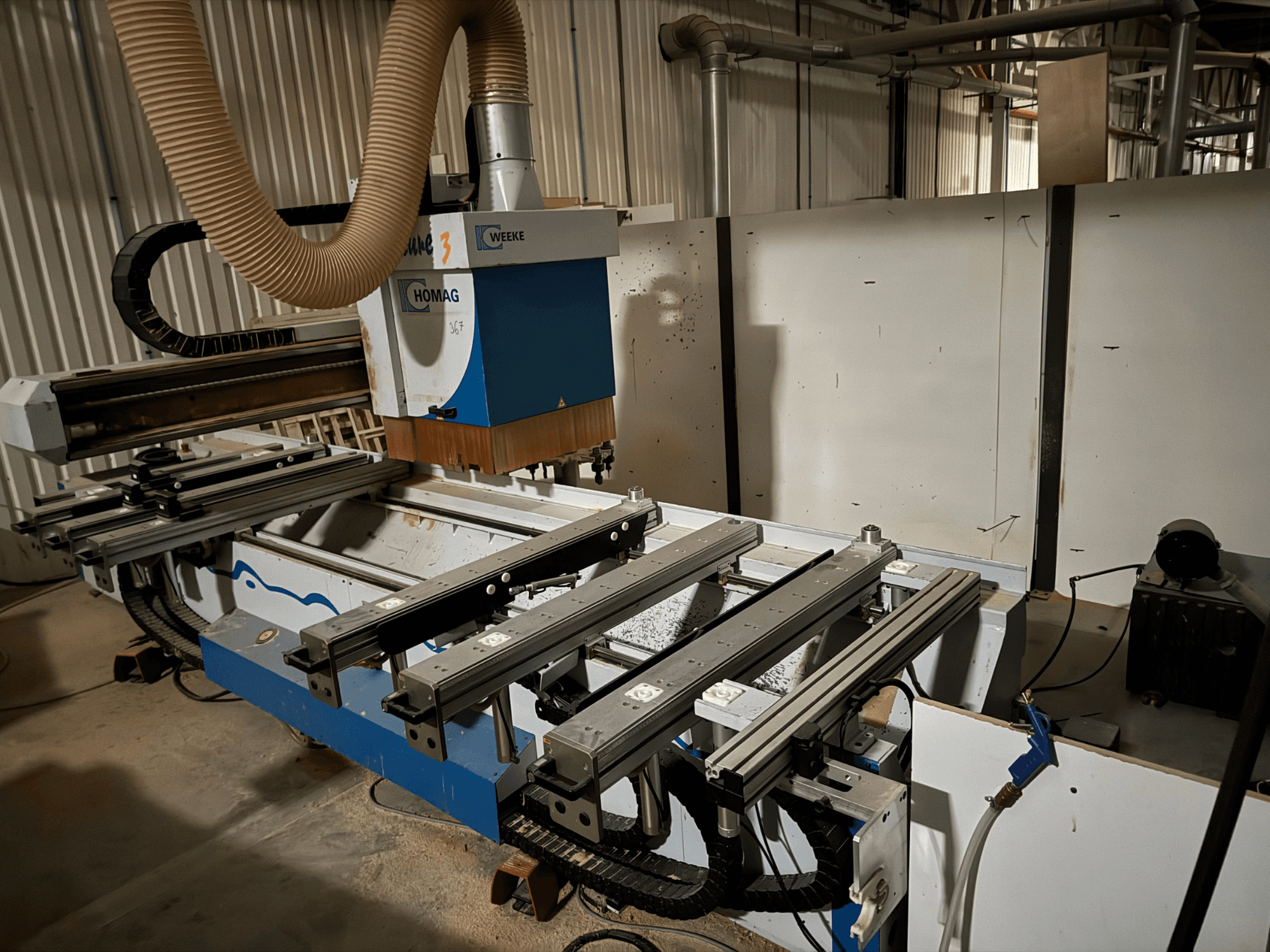 HOMAG CNC-gép kék-fehér kivitelben, oldalnézetben, csúszó sínekkel, porelszívó rendszerrel és szerelt szerszámokkal.
