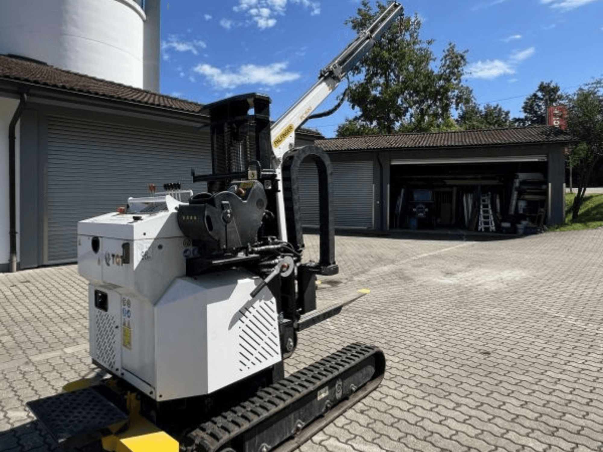 TGI építőipari minidaru, oldalnézet, a sínek és a szerelt gém bemutatása, egy garázs mellett téglafelületen parkolva.