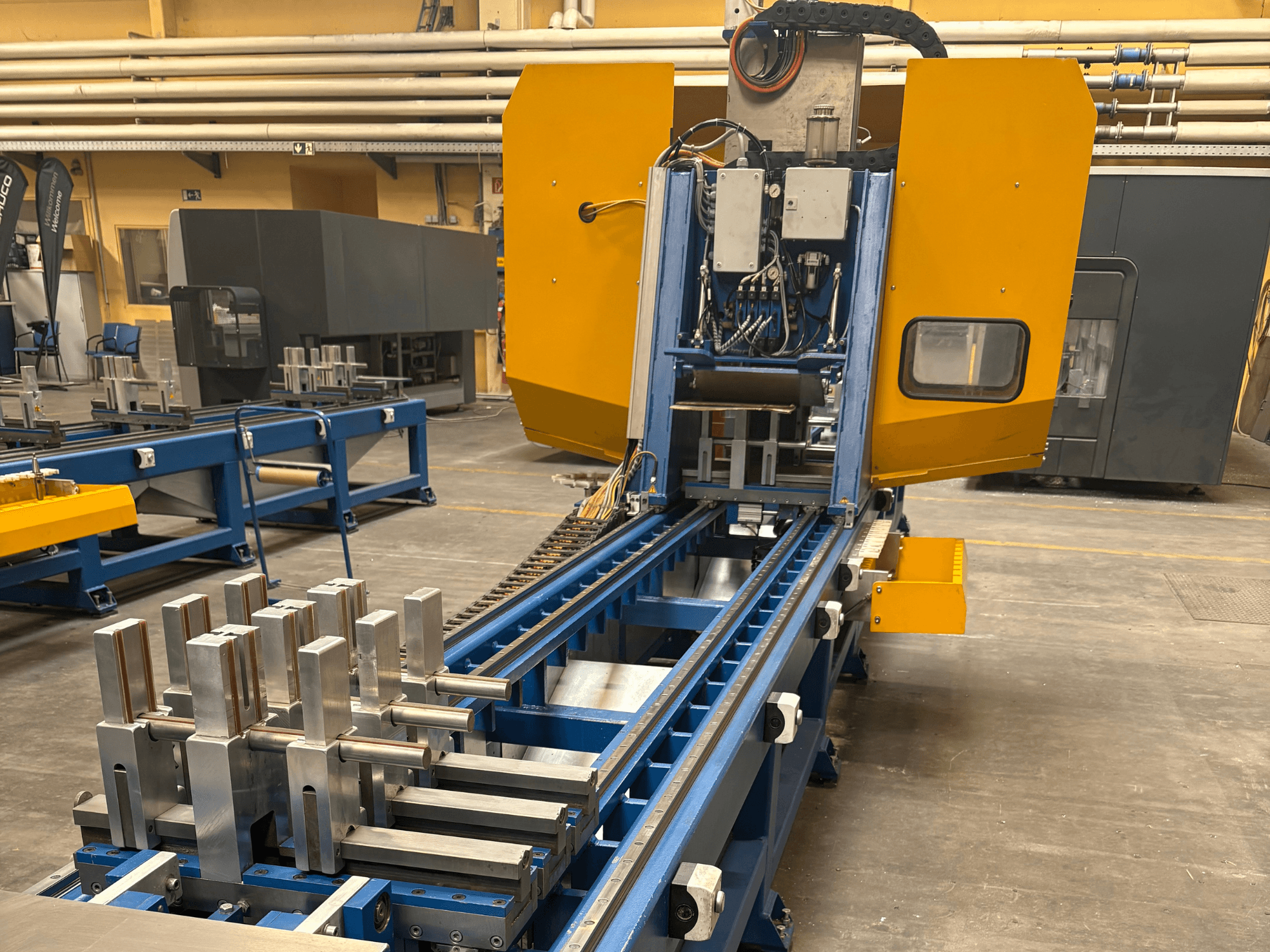 A SCHÜCO PBX AL univerzális megmunkálóközpont elülső nézete, amely fém munkadarabokat mutat a kék megmunkálóágyon.