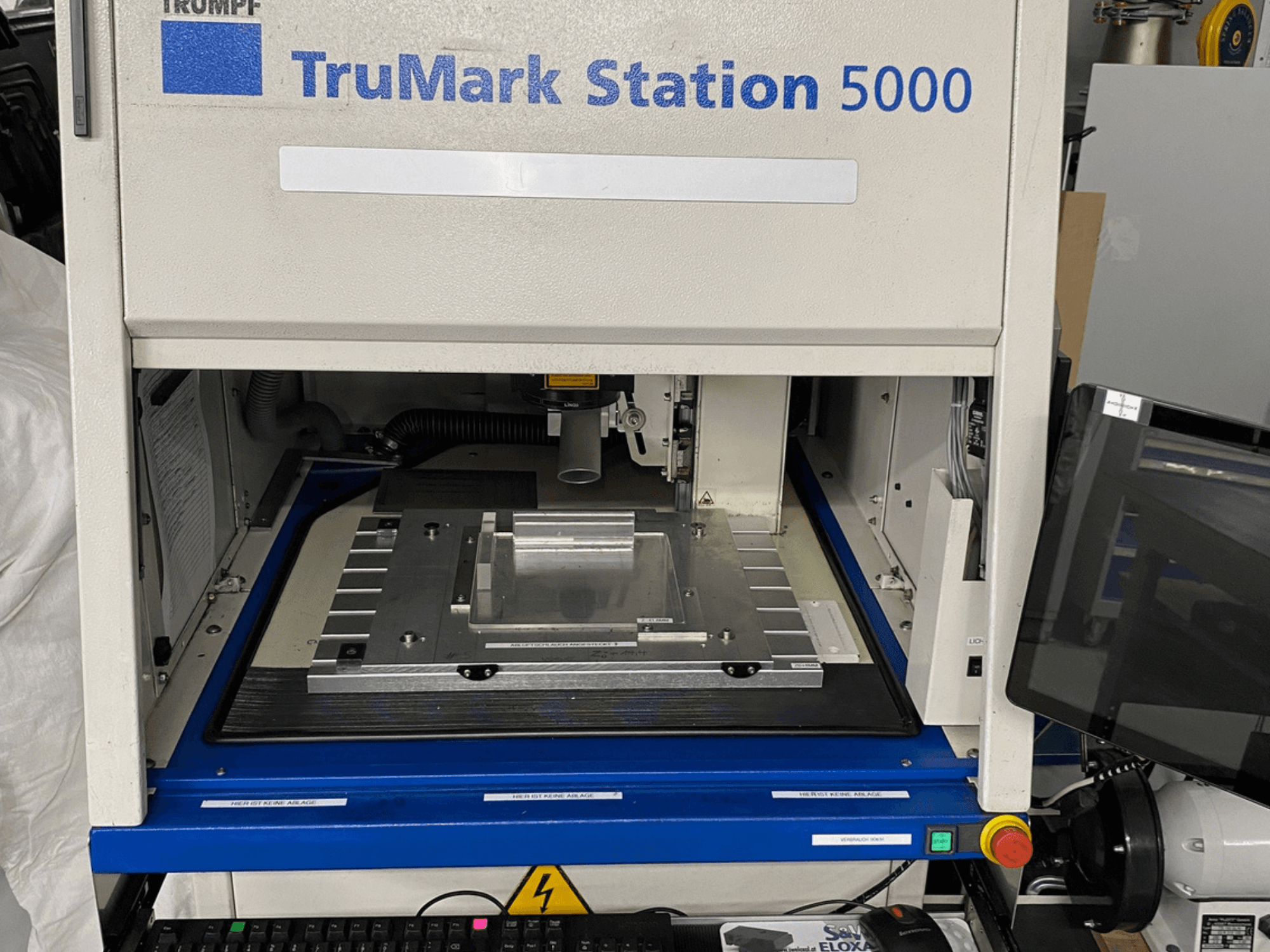A TruMark Station 5000 lézeres jelölőgép előlapja, amely a munkaasztalt, a kezelőszerveket és a felügyeleti képernyőt mutatja.