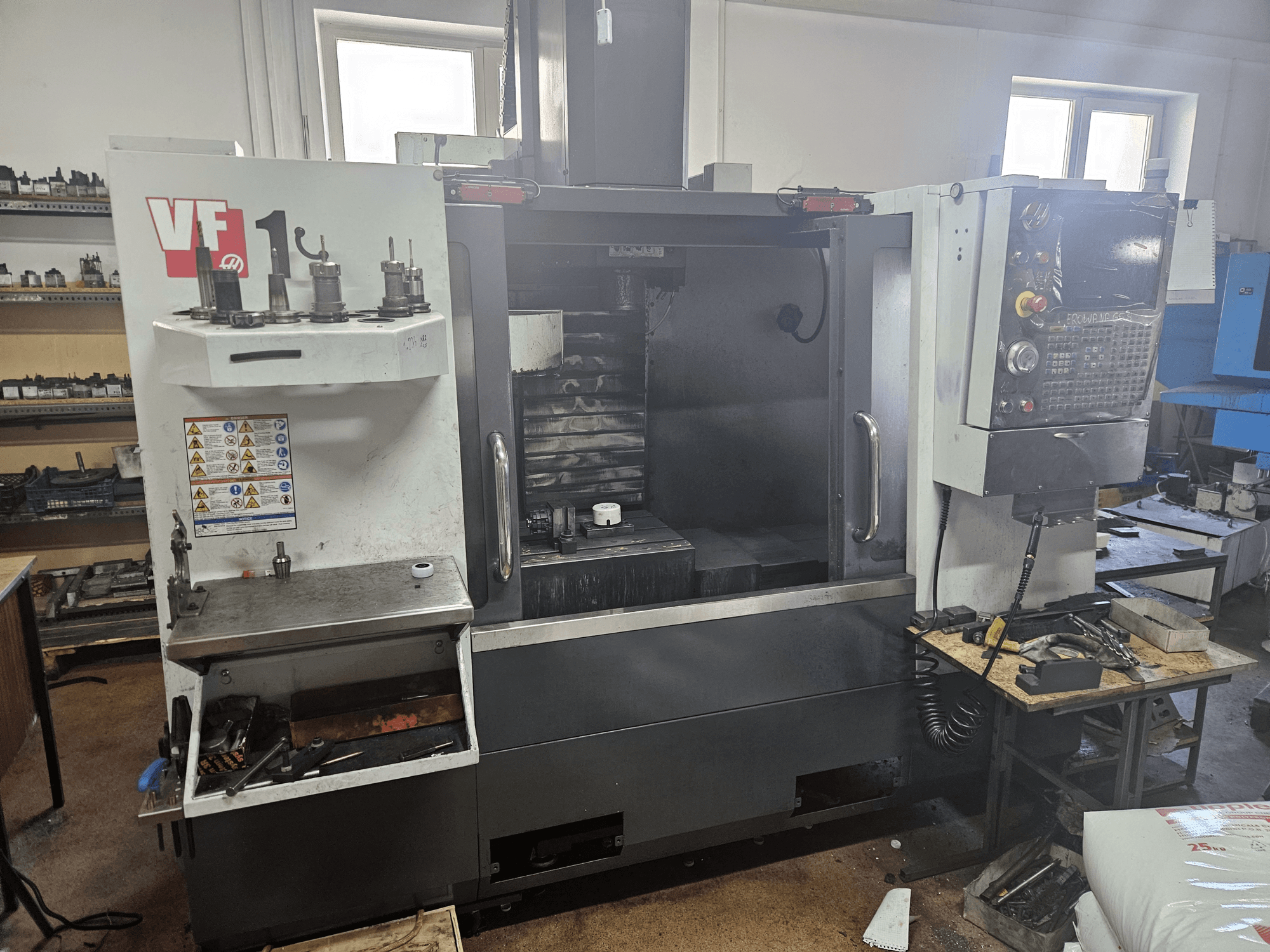 HAAS VF-1 függőleges megmunkálóközpont, elölnézetben, szerszámokkal az oldalán, a vezérlőpanel látható, háttérben a munkaterület.