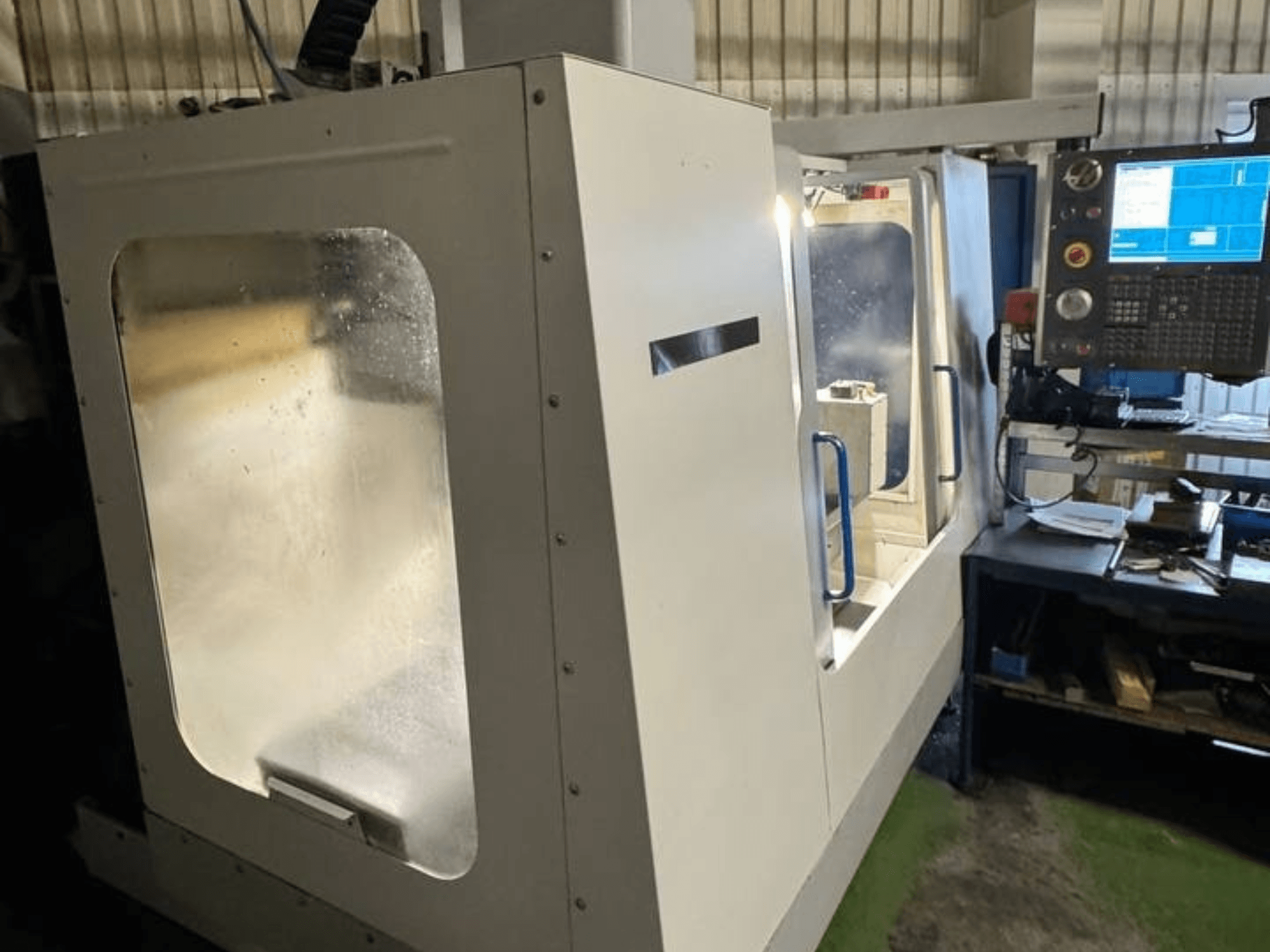 HAAS VCE 750 függőleges megmunkálóközpont oldalnézetben, vezérlőpanellel és átlátszó biztonsági burkolattal.