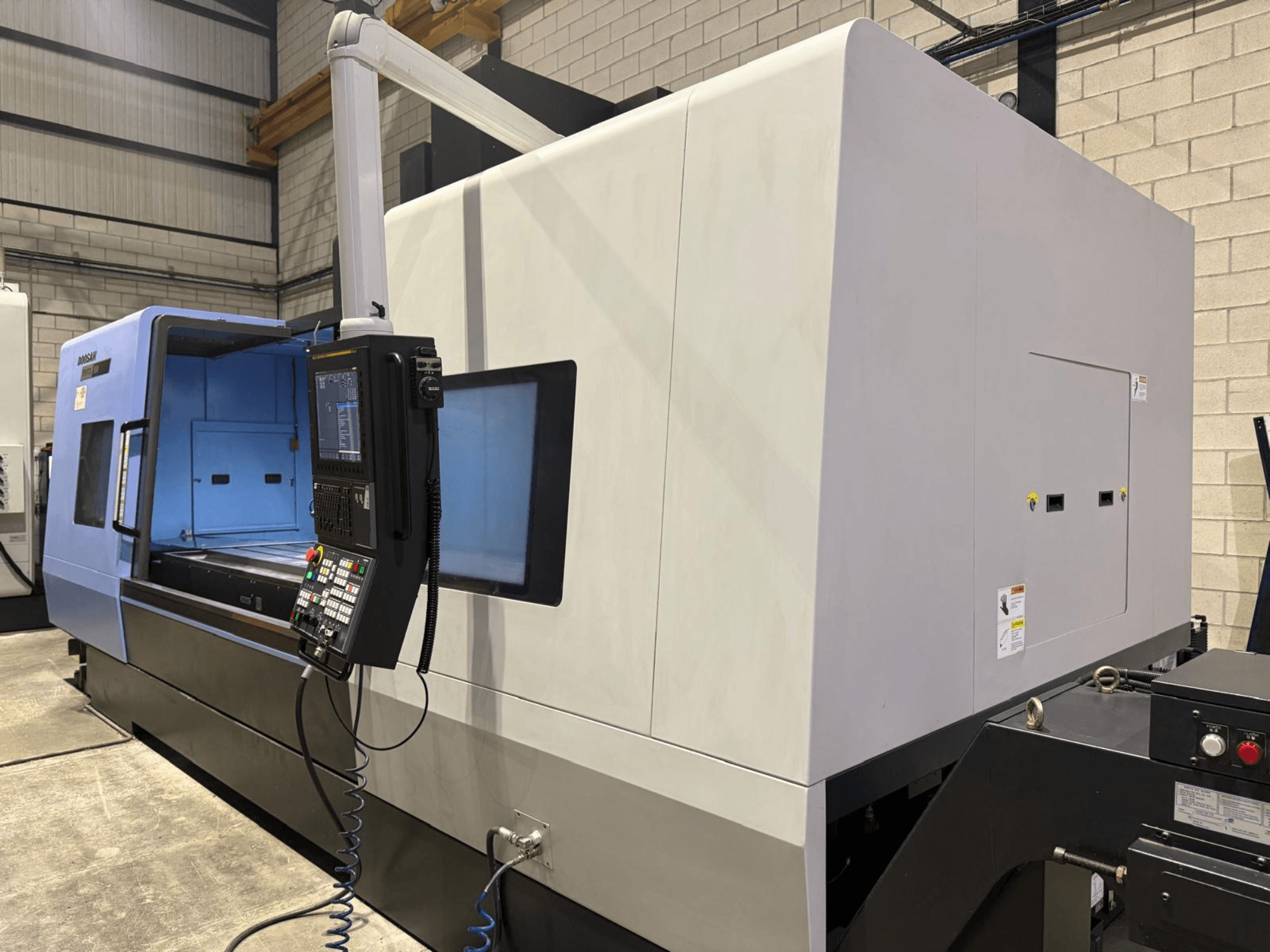 Ipari CNC eszterga, kék és szürke külső, előlnézet; gombokkal és kijelzővel ellátott vezérlőpanel a pontos műveletekhez.