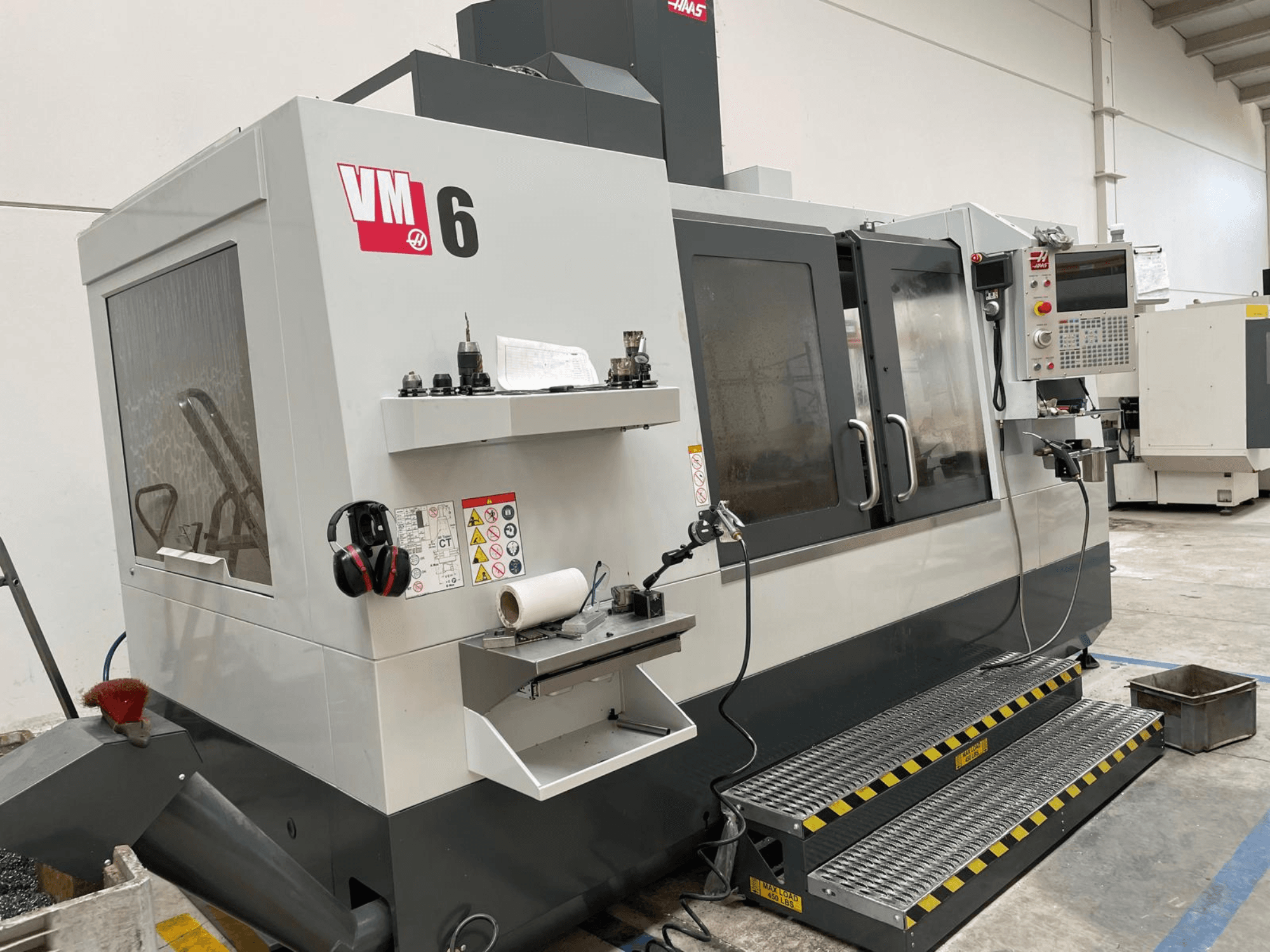 Haas VM-6 függőleges megmunkálóközpont, elölnézetben a vezérlőpanel, a szerszámtartók és a biztonsági berendezések.