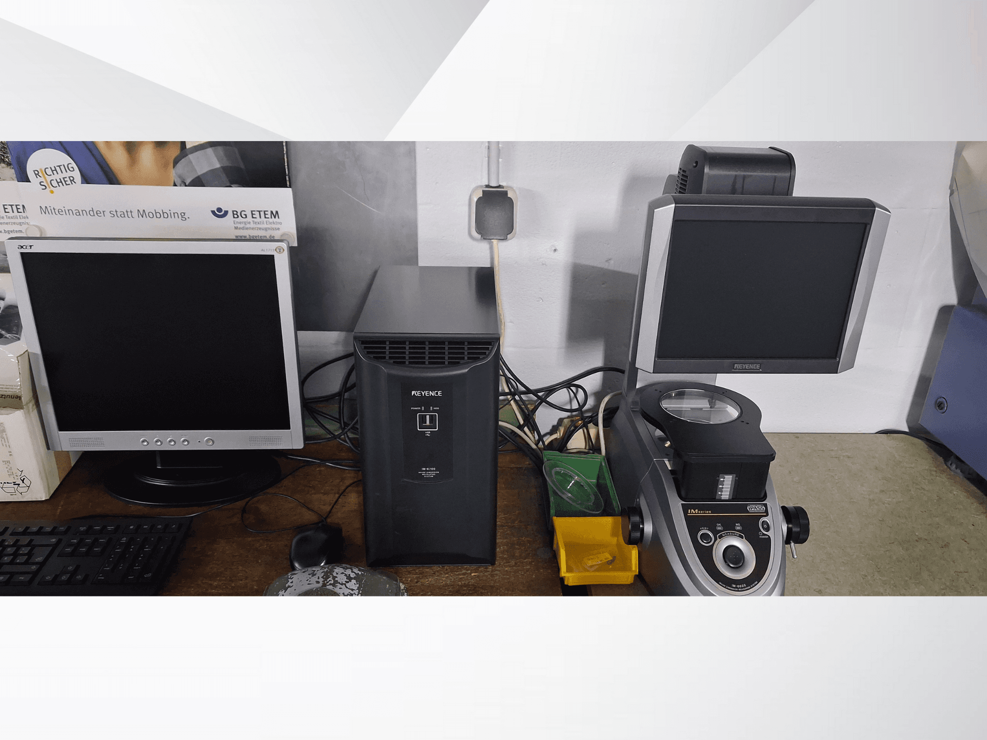 Két számítógép-monitor, egy Acer és egy Keyence, egy fekete eszköz és egy mikroszkóp mellett, szemből nézve.