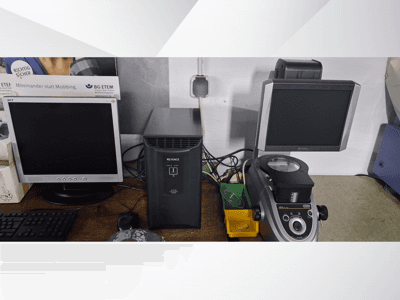 Két számítógép-monitor, egy Acer és egy Keyence, egy fekete eszköz és egy mikroszkóp mellett, szemből nézve.