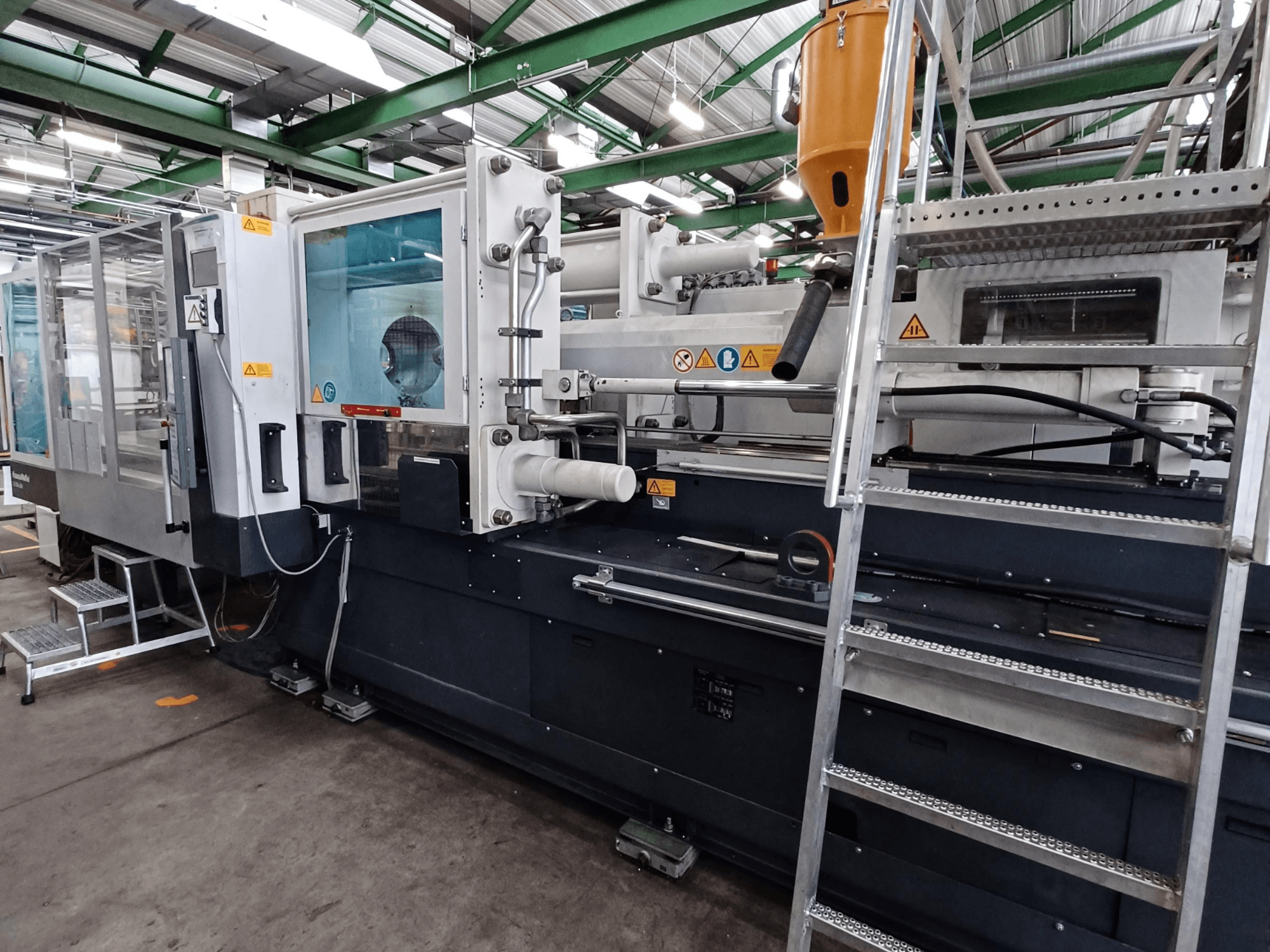 Ipari fröccsöntőgép tiszta elülső nézettel, amelyen a márkajelzések, a vezérlőpanel és az anyagtartály látható.