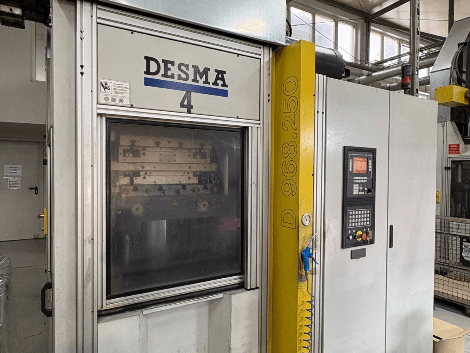 Kloeckner Desma 968.250 függőleges fröccsöntőgép, elölnézetben a vezérlőpanel és a gép részletei.