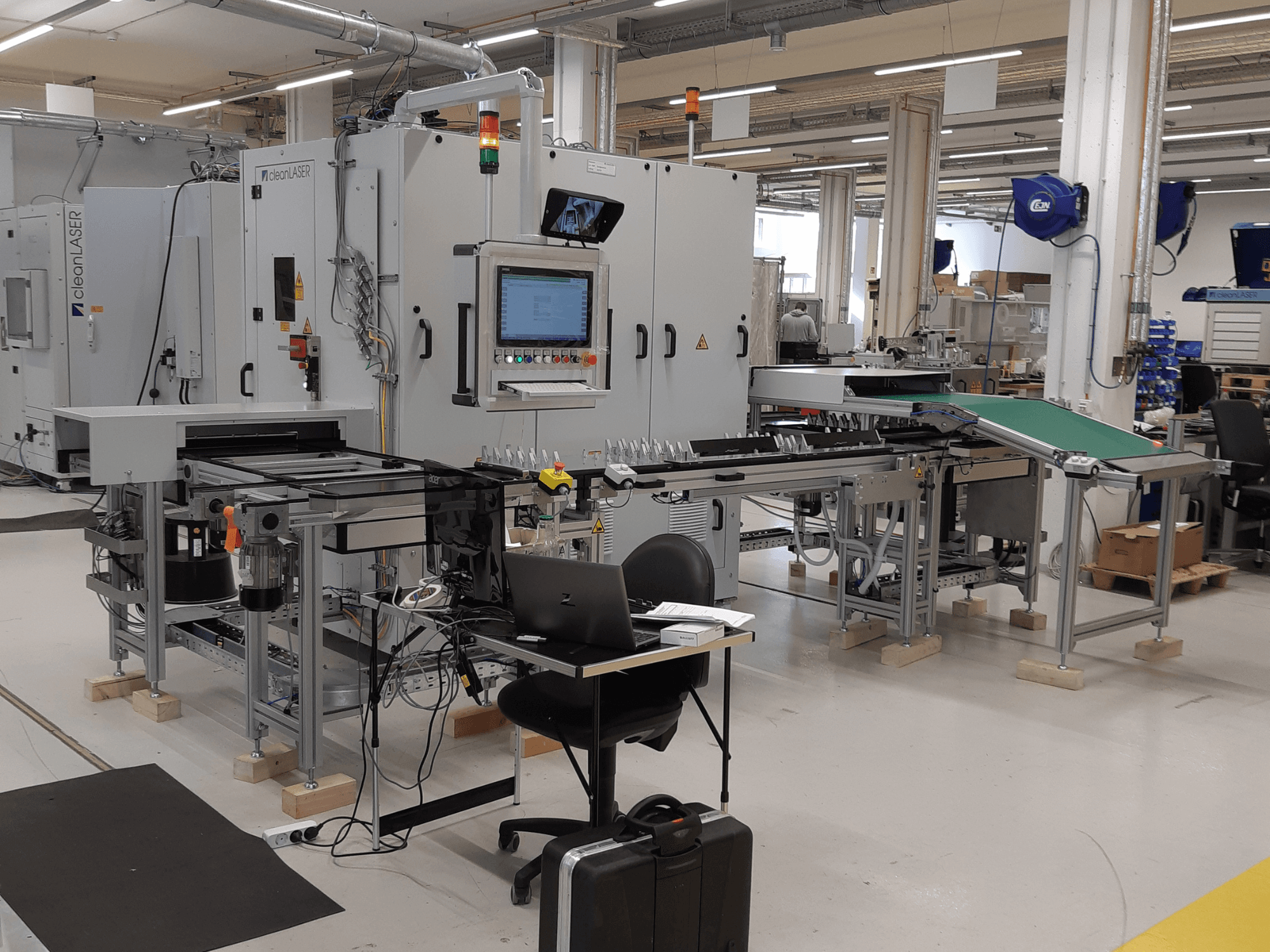 CLEAN LASER clean CELL 3220 CL600 szerszámgép, elölnézet, a vezérlőpanellel, a szállítószalaggal és a munkaterülettel együtt, műhelyi környezetben.