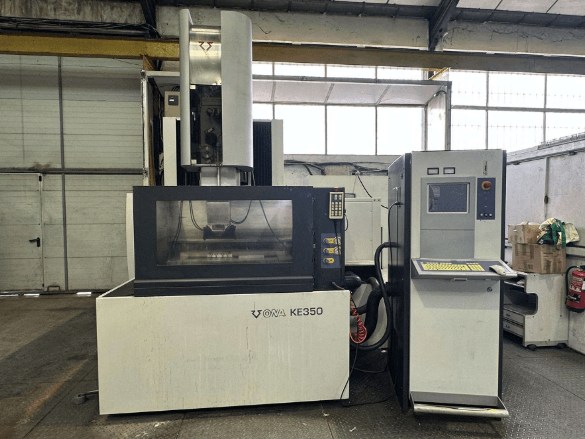 Az ONA KE350 CNC-gép előlapja a vezérlőpanellel, a kijelzővel és a különböző gombokkal, ipari környezetben.