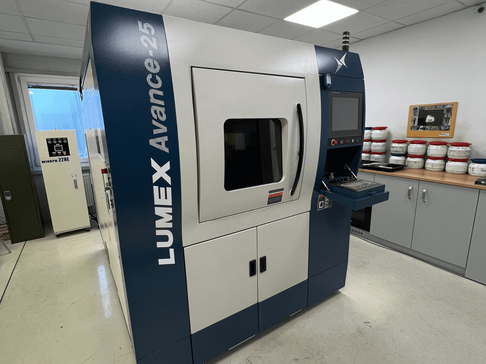 LUMEX Avance-25 3D nyomtató laboratóriumi környezetben, előlnézet. Vezérlőpanel a képernyővel és a gombokkal, háttérben a berendezés.