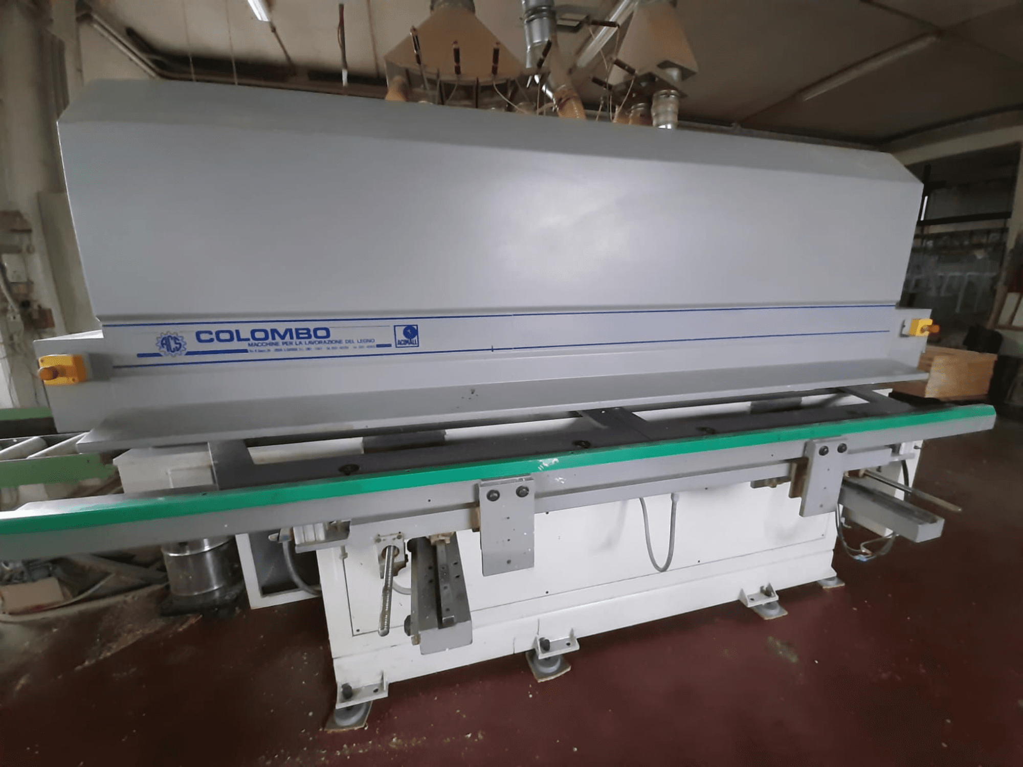 Colombo fafeldolgozó gép, elölnézetben, hosszú zöld asztallal, vezérlőgombokkal és szürke testtel, kék ékezetekkel.