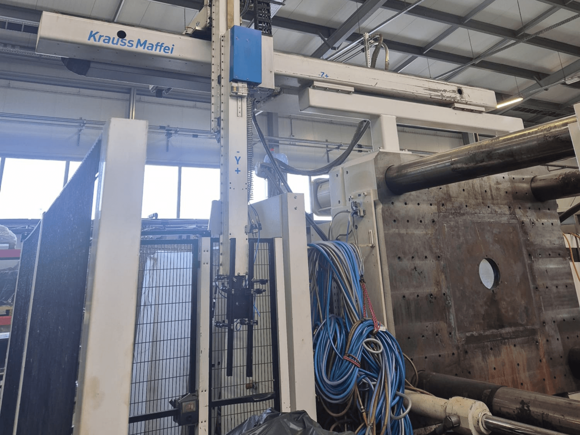Krauss Maffei 1300-12000 MX hidraulikus fröccsöntőgép, elölnézet mechanikus karokkal és hidraulikus csatlakozásokkal.