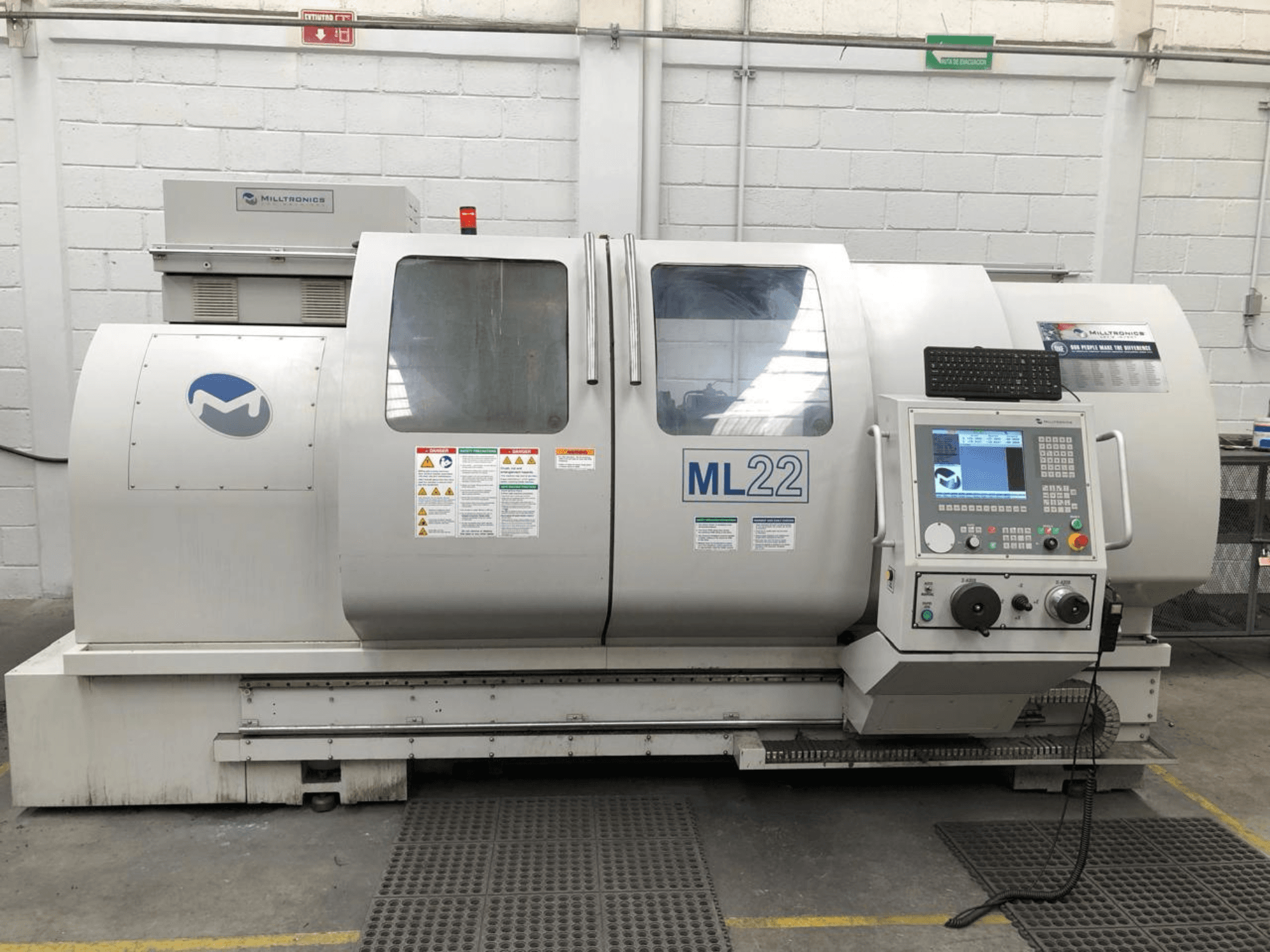 Függőleges megmunkálóközpont MILLTRONICS RH 20, elölnézetben a kezelőpanel, a márka logója és a gépen lévő biztonsági címkék.
