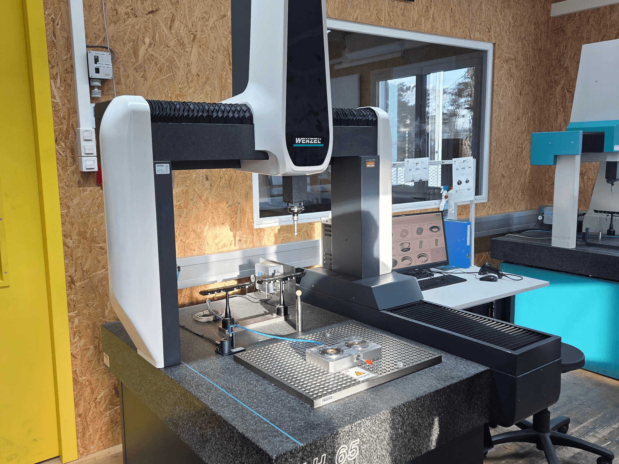 Wenzel LH 65 koordináta-mérőgép laboratóriumi berendezésben, elölnézetben, mérőeszközök és egy monitor megjelenítésével.