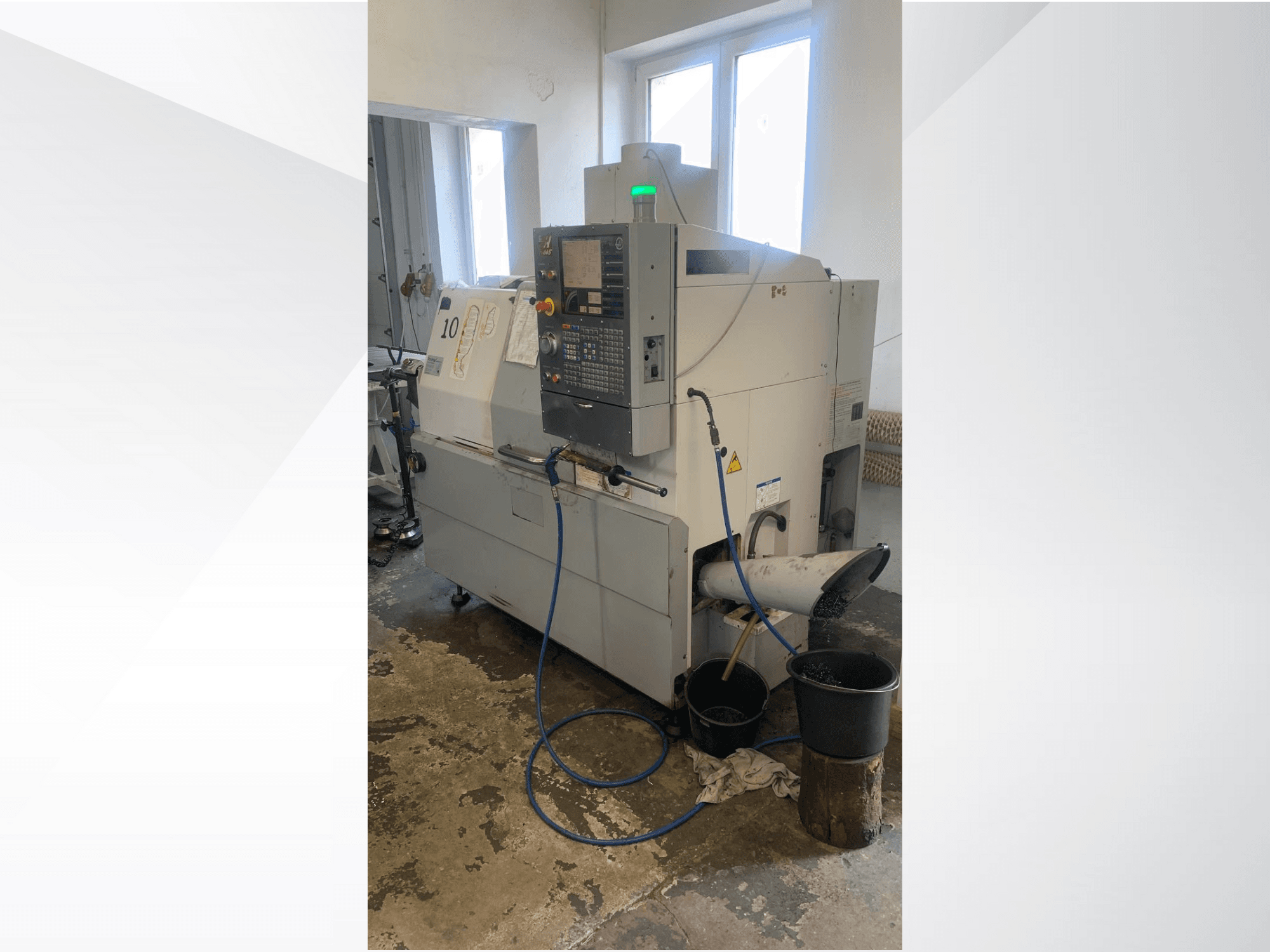 Haas CNC-gépmodell vezérlőpanellel, oldalnézetben, hűtőfolyadék-vezetékkel, hulladékcsúszdával és az alatta lévő tárolóedényekkel.