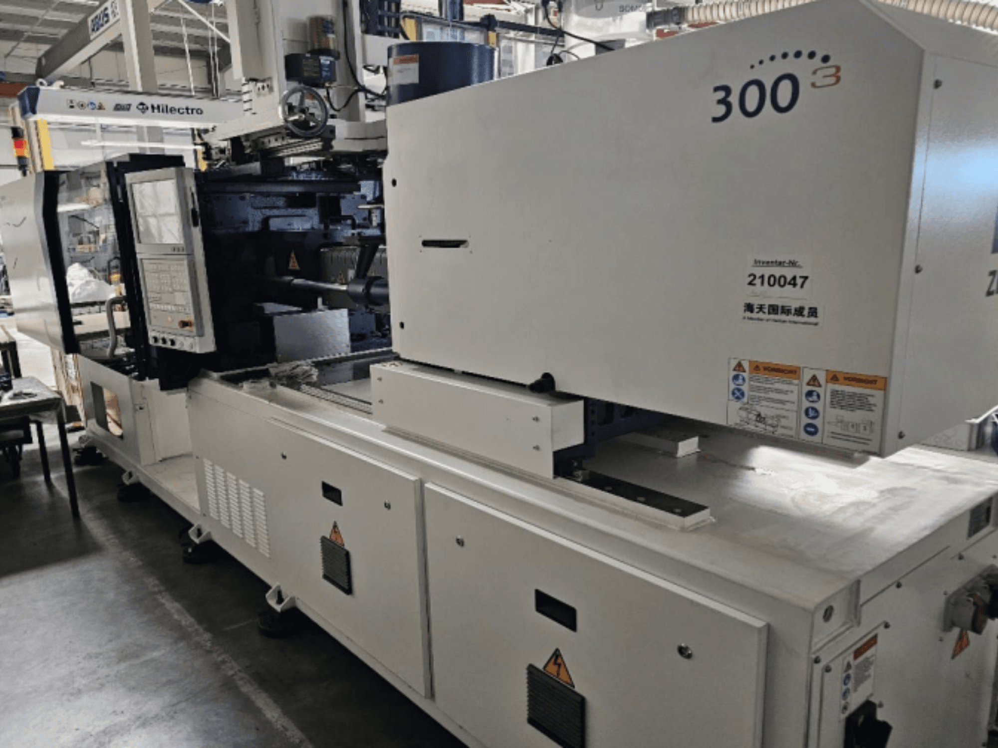 Zhenjing márkájú fröccsöntőgép, 300-as modell, elölnézet a vezérlőpanellel és a biztonsági figyelmeztető címkékkel.