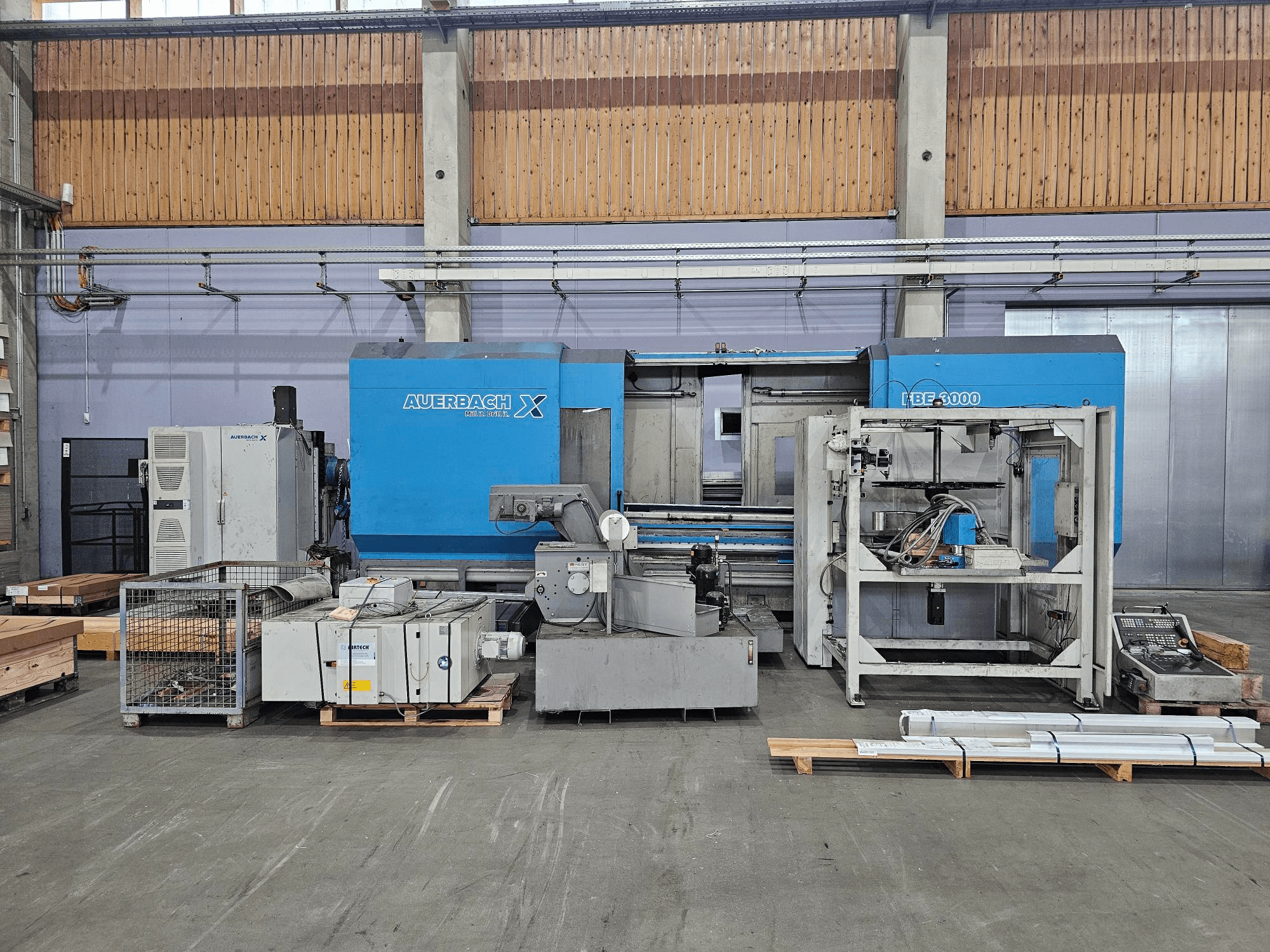 Auerbach X LBF-3000 gép gyári környezetben, oldalnézetben, szürke és kék alkatrészekkel, látható vezérlőpanellel.