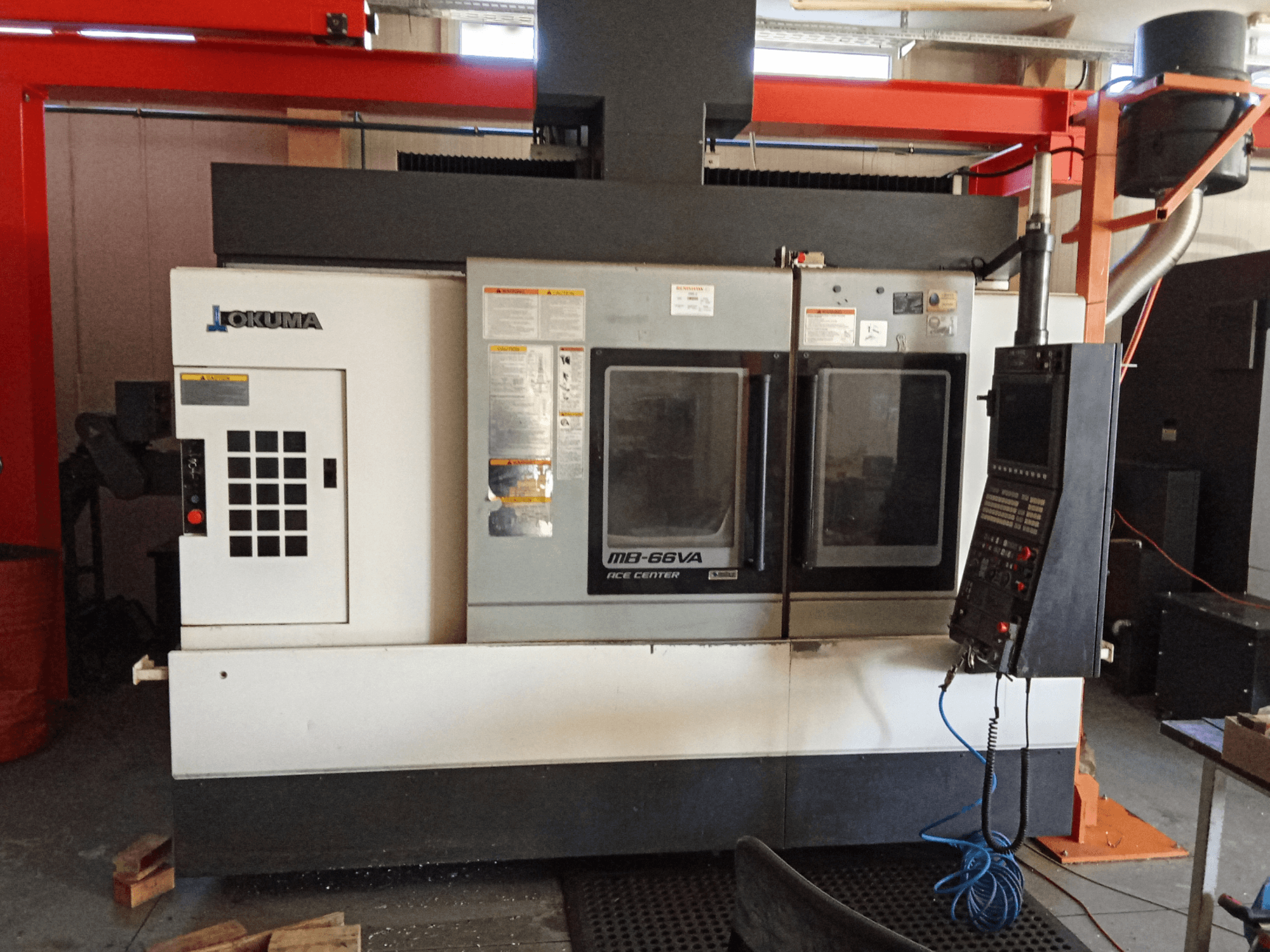 Okuma MB-66VA függőleges megmunkálóközpont, elölnézetben a vezérlőpanel és a szerszámokhoz való hozzáférést biztosító kettős ablakok.