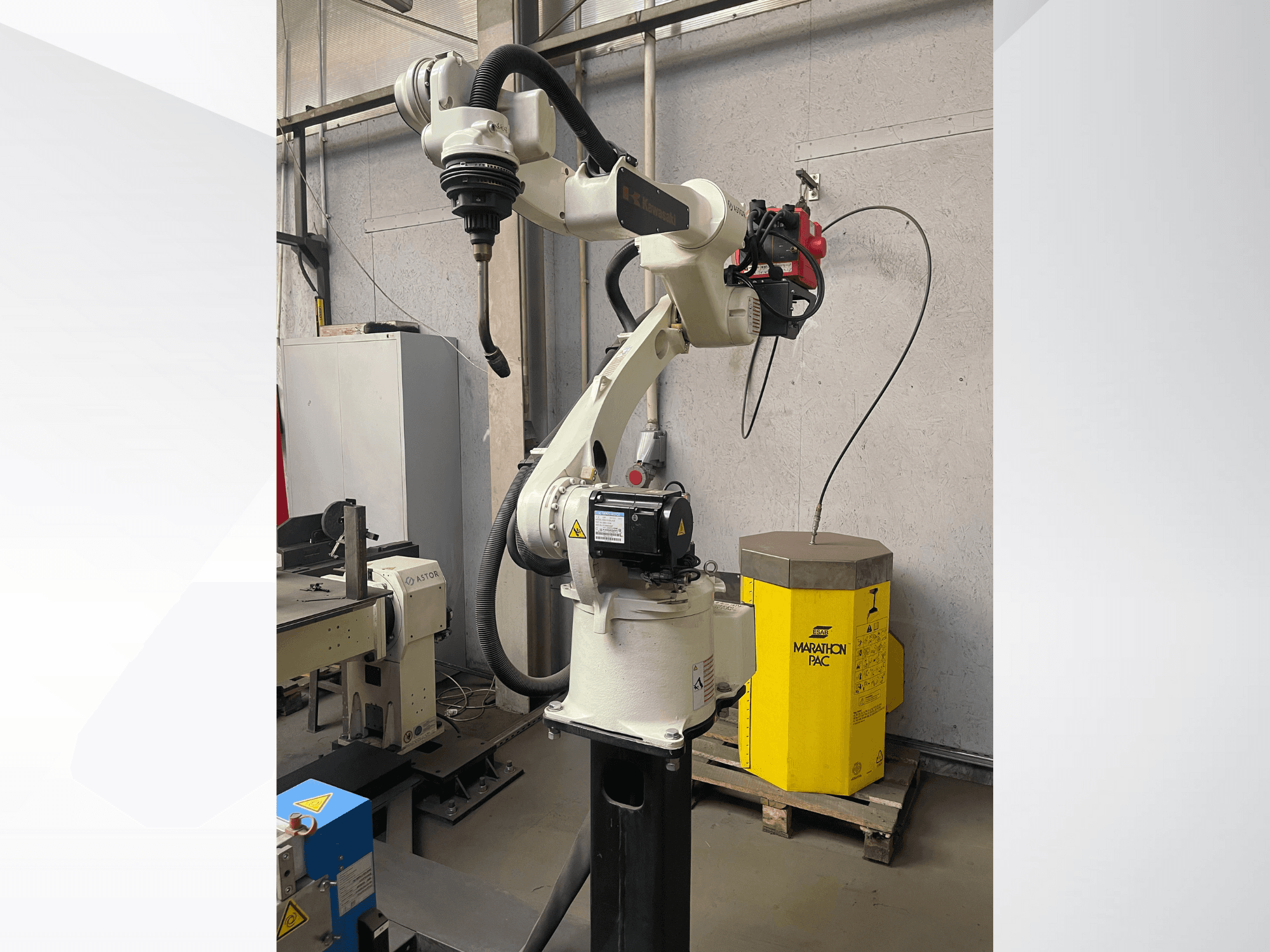 Kawasaki robotkar oldalnézetből, a felszerelt szerszámtartóval, a háttérben a sárga erőforrással.