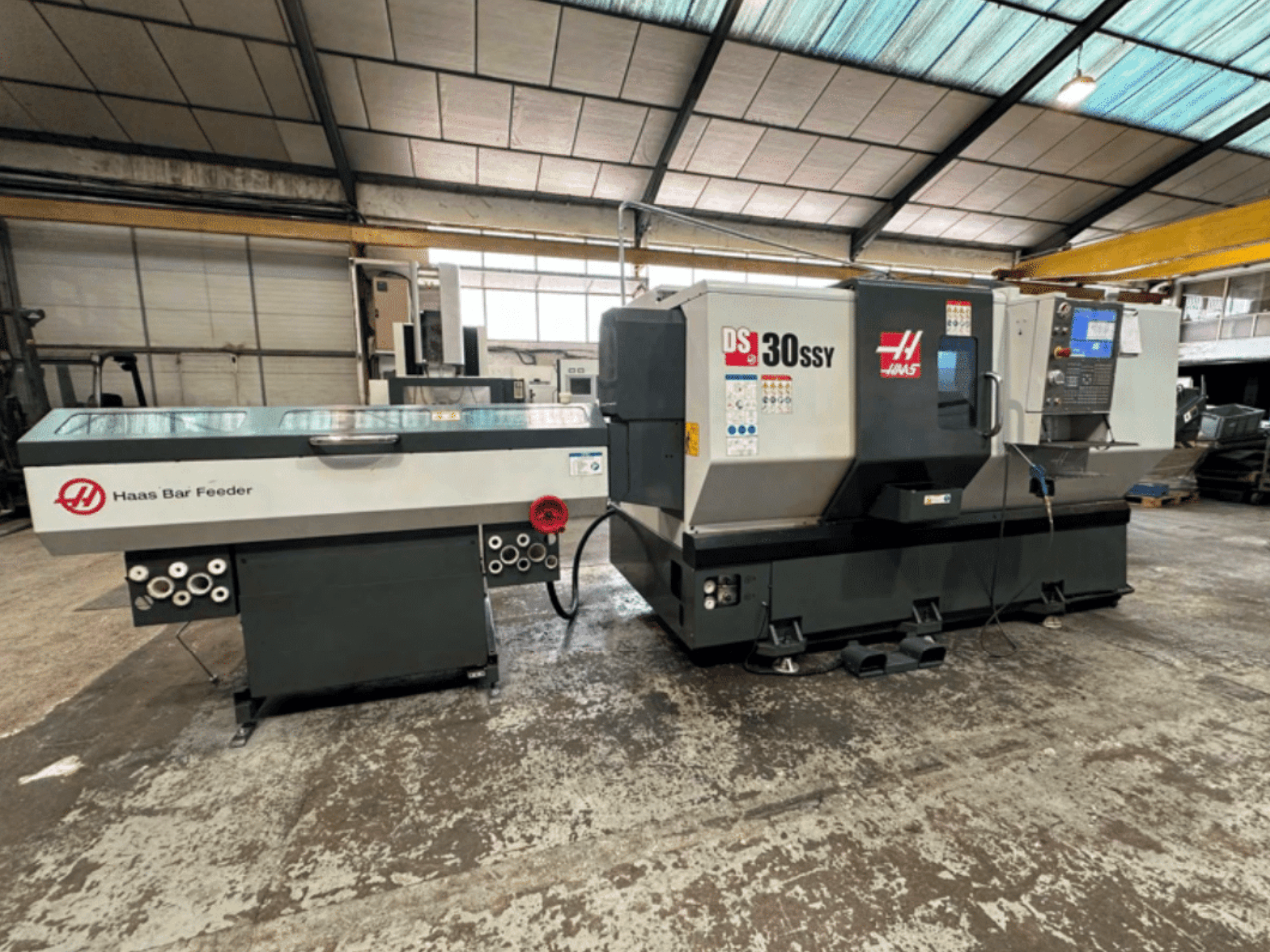 Haas DS-30SSY CNC eszterga Haas rúdadagolóval, oldalnézet a vezérlőpanel és az adagoló mechanizmus műhelyben.