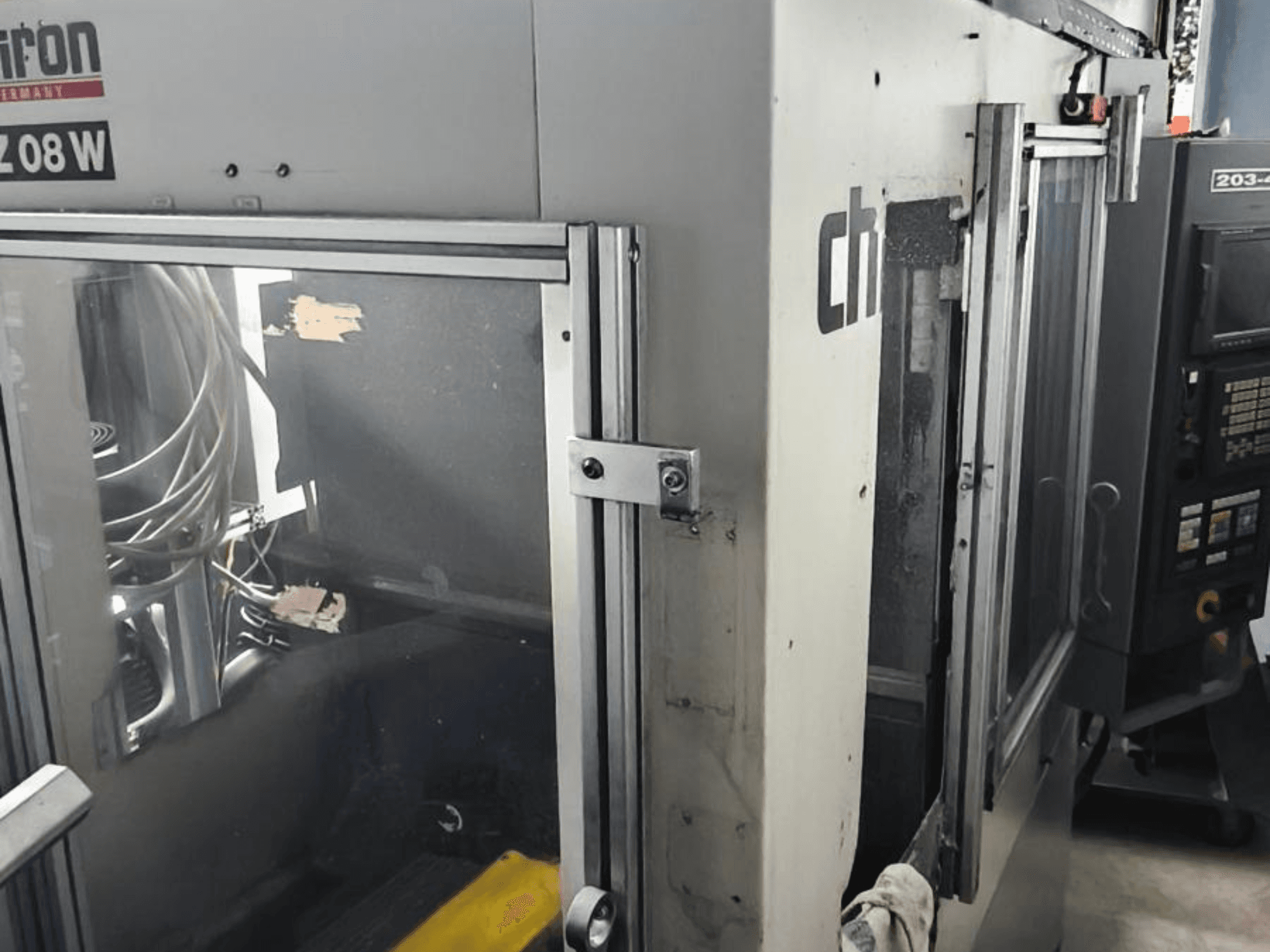 Függőleges megmunkálóközpont CHIRON FZ 08 W, elölnézetben a vezérlőpanel és a részben nyitott ajtók, látható belső alkatrészekkel.