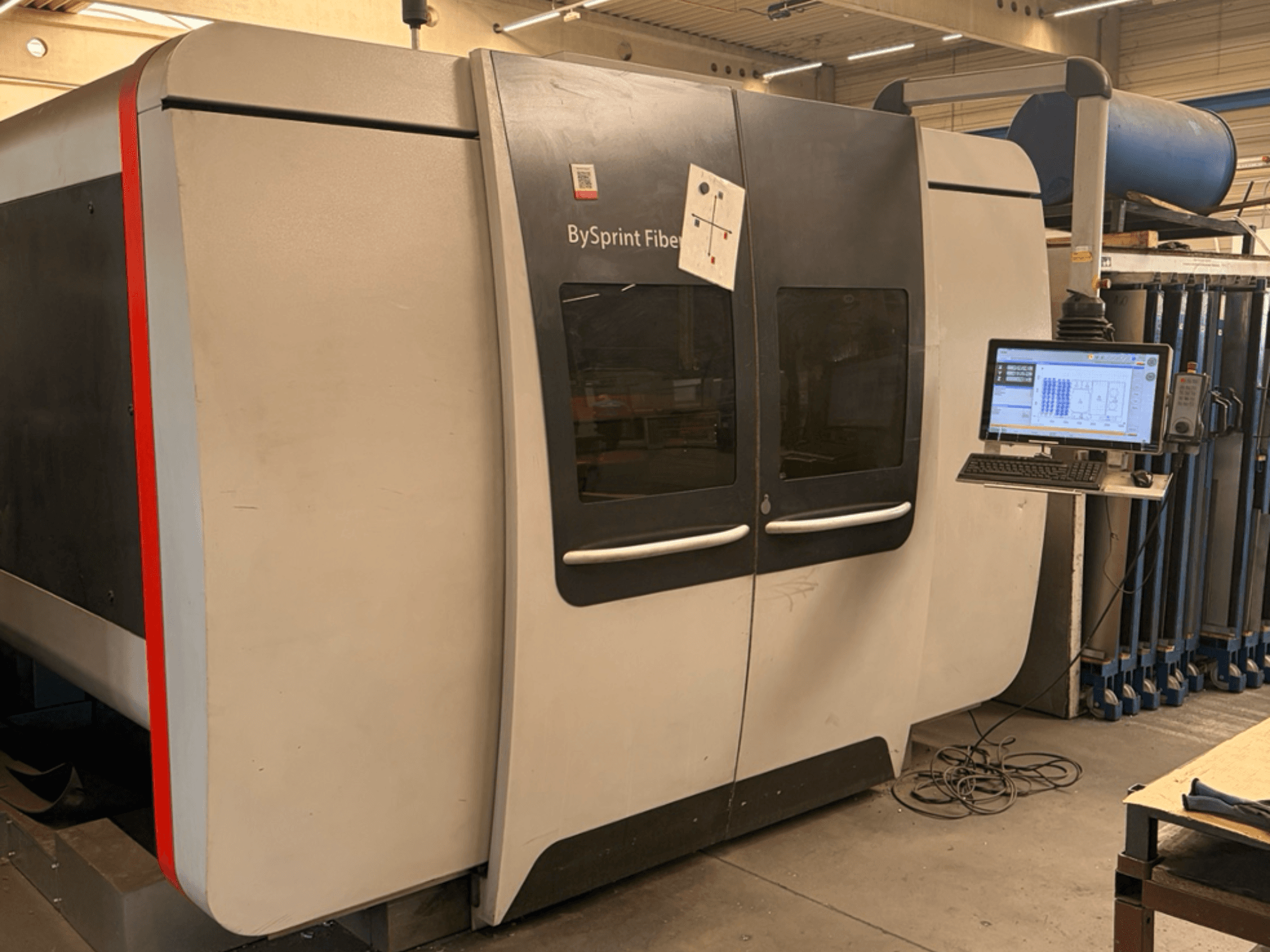 Bystronic BySprint Fiber 3015, a száloptikás lézervágó gép elölnézete érintőképernyős vezérlőpanellel és ipari környezetben.