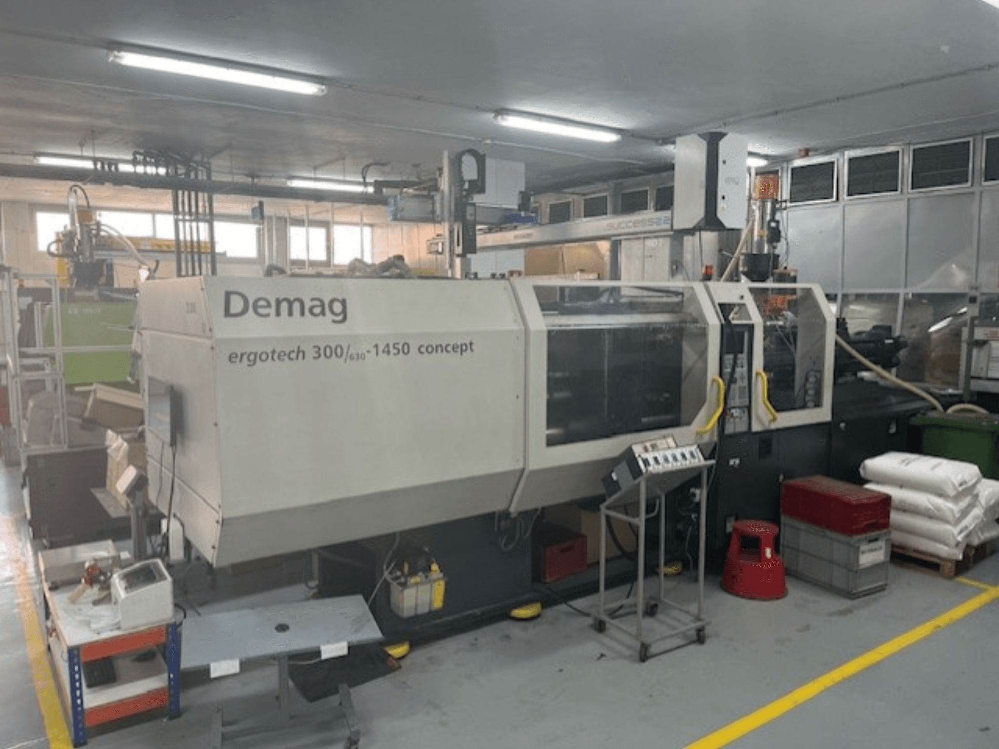 Demag ERGOTECH CONCEPT 3000-1450 hidraulikus fröccsöntőgép, elölnézetben, kezelőszervekkel és a közelben lévő anyagokkal.