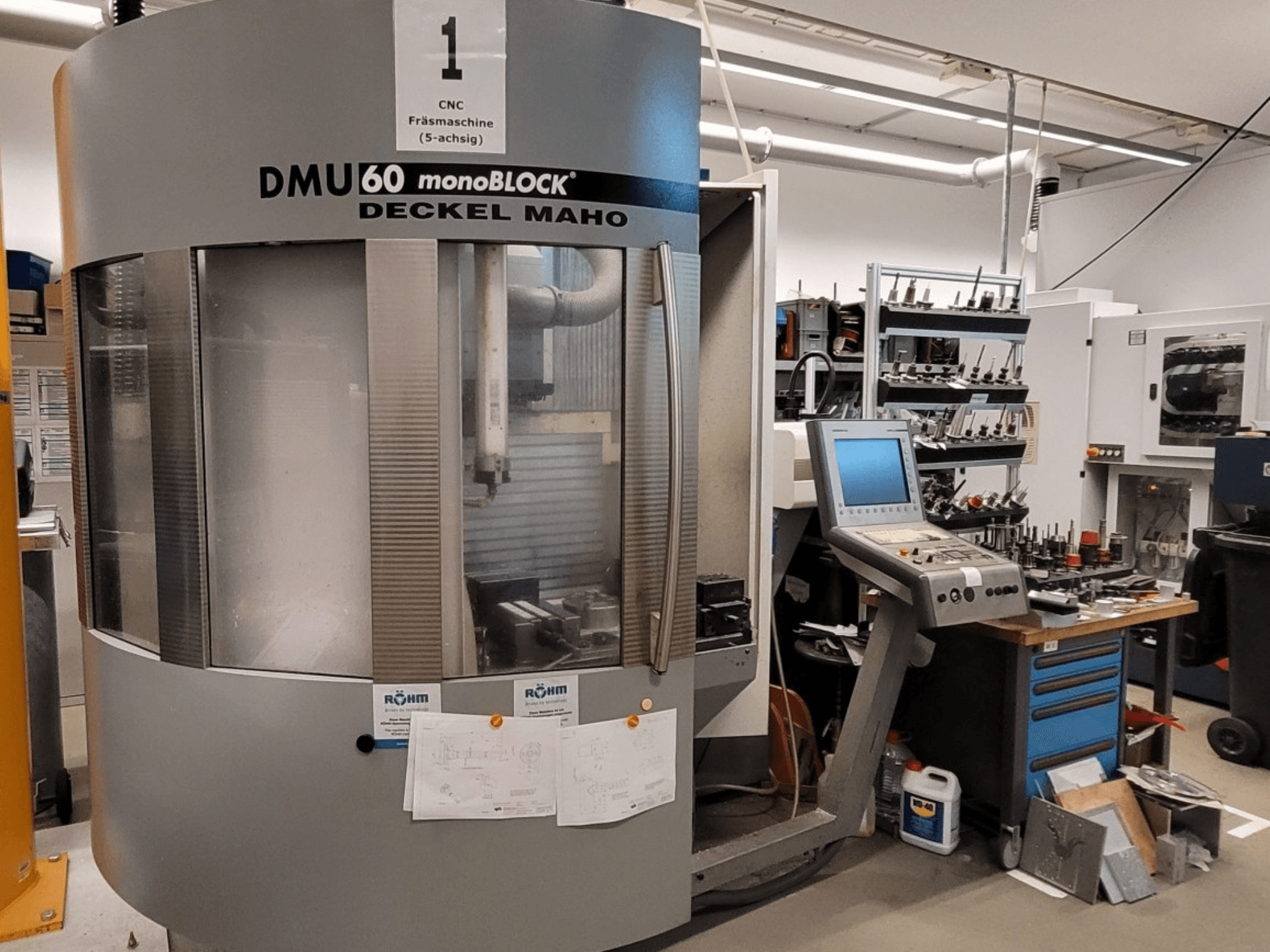 CNC marógép DECKEL MAHO DMU 60 monoBLOCK elölnézetben, mellette a vezérlőpanel és a szerszámtároló.
