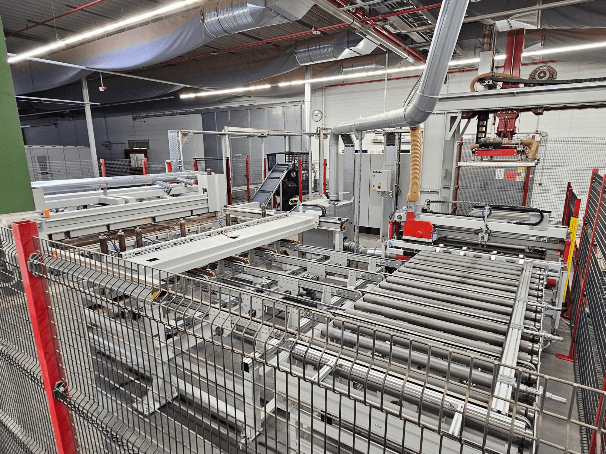 HOLZMA HPP81-3200 lemezfűrész elölnézetben, szállítógörgőkkel és gépalkatrészekkel egy műhelyben.