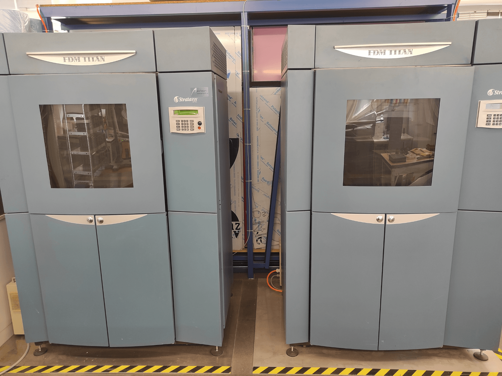 A Stratasys FDM TitanTI 3D-nyomtatója, elölnézetből, kettős ajtókkal és vezérlőpanellel, ipari környezetben.