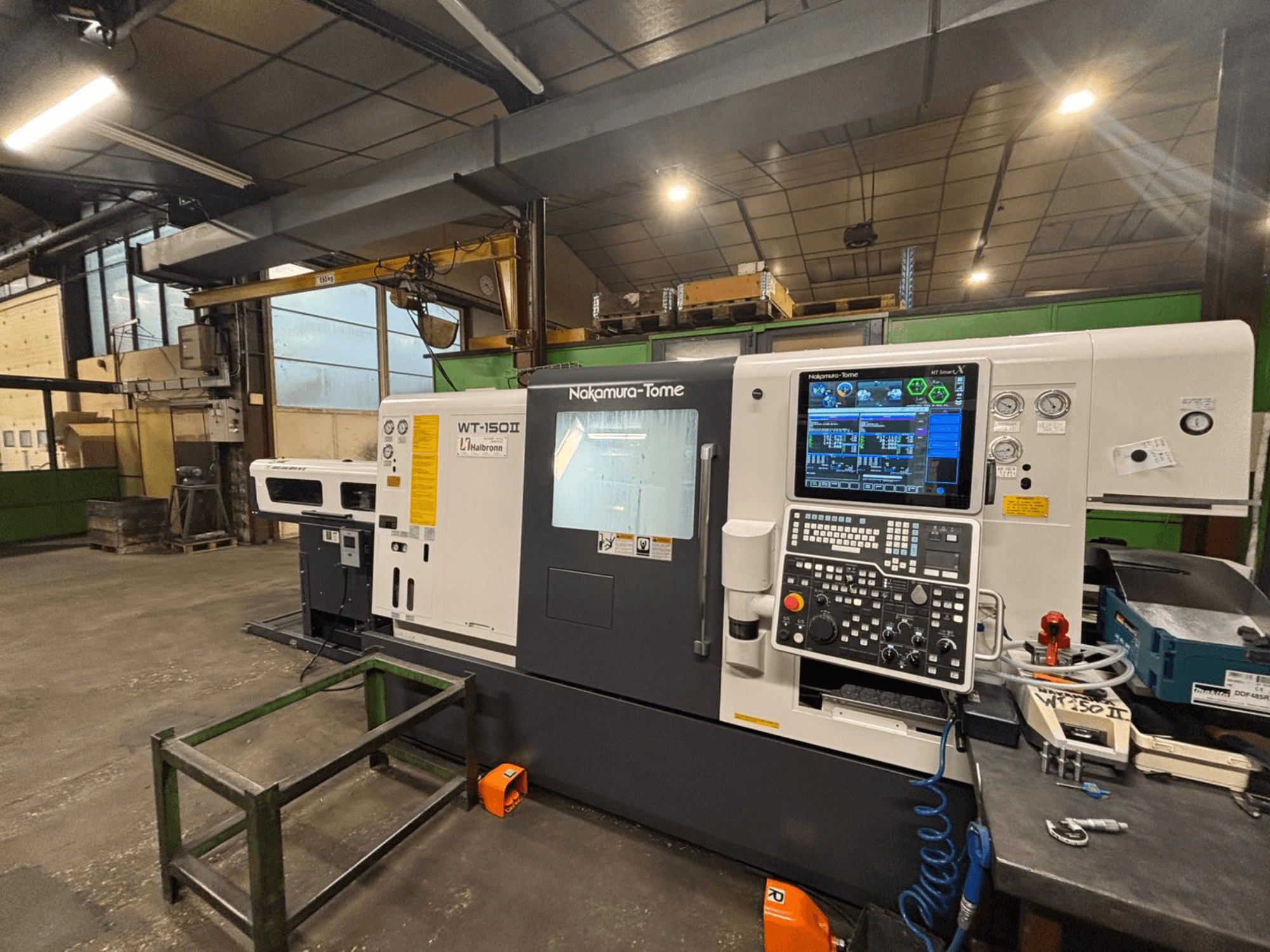 Nakamura-Tome WT-150II gép, elölnézet, a kezelőpanel és a szerszámok láthatóak egy műhelyben, egy munkapadon.