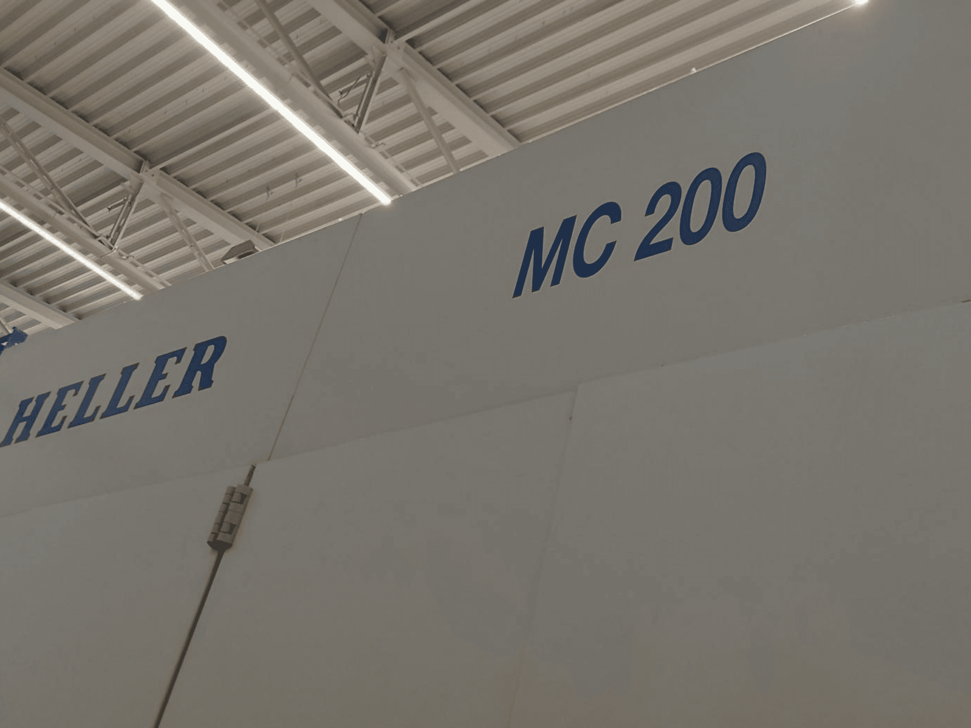 Heller MC 200 vízszintes megmunkálóközpont, oldalnézetből, a márka és a modell kék betűkkel kiemelve fehér felületen.