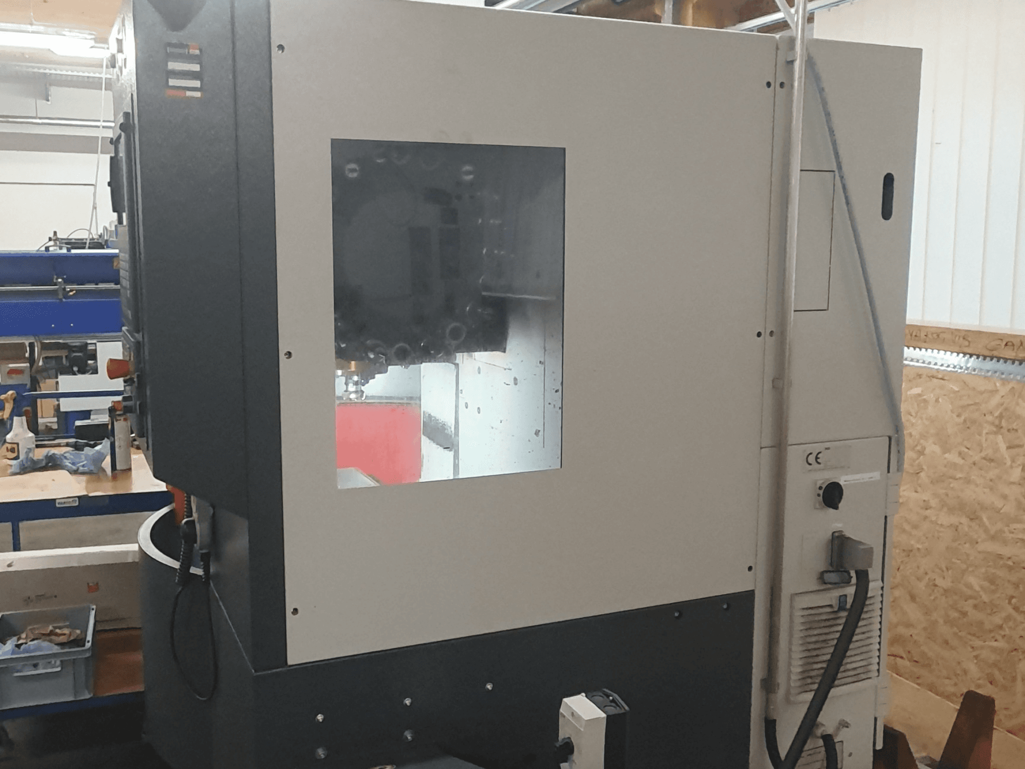 Egy fémmegmunkáló gép oldalnézetben, látható vezérlőpanellel, nagy látóablakkal és bonyolult belső alkatrészekkel.