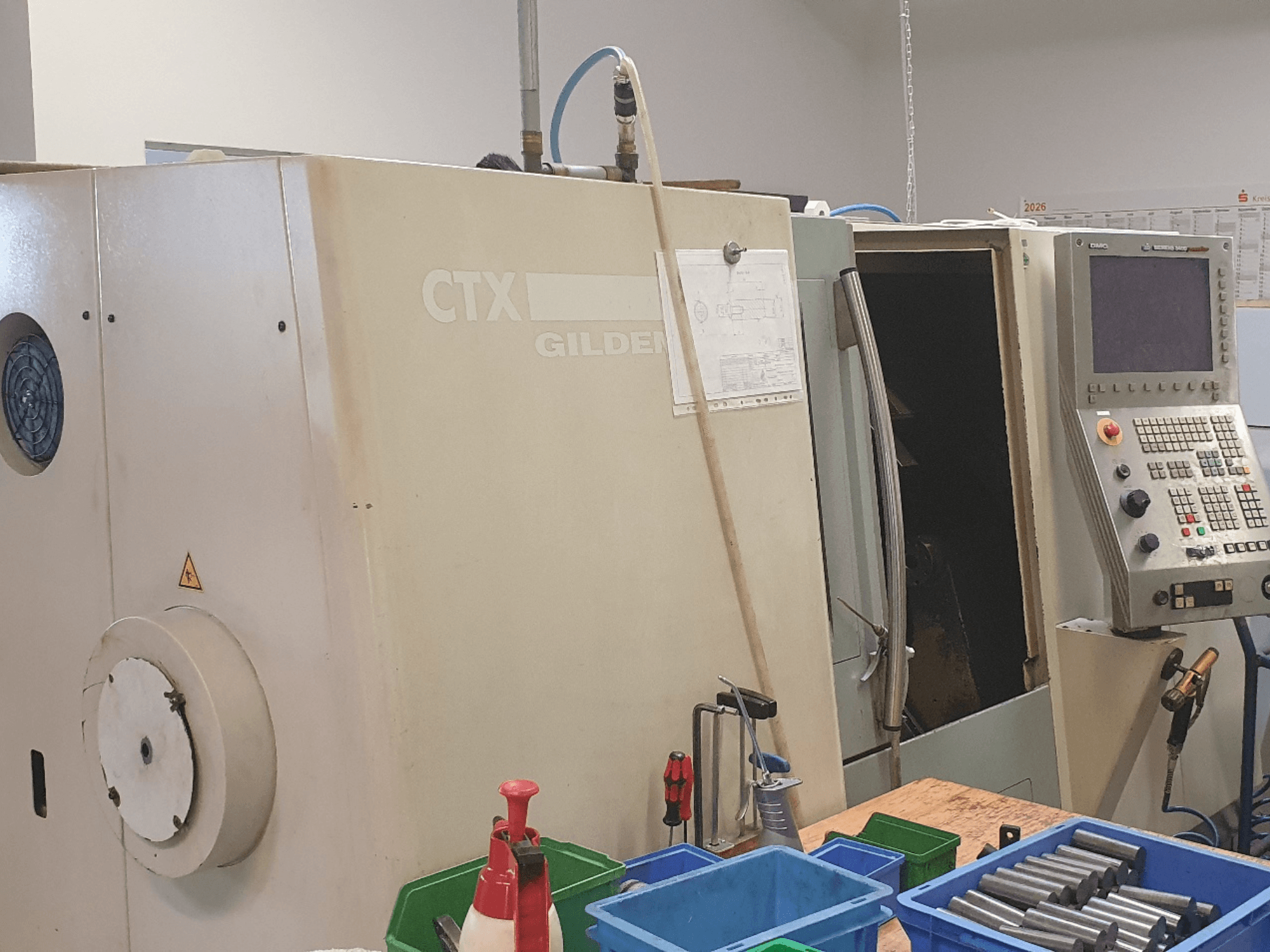 A DMG GILDEMEISTER CTX 310 vízszintes eszterga elölnézete, látható a vezérlőpult, az előtérben szerszámok és tárolóedények.