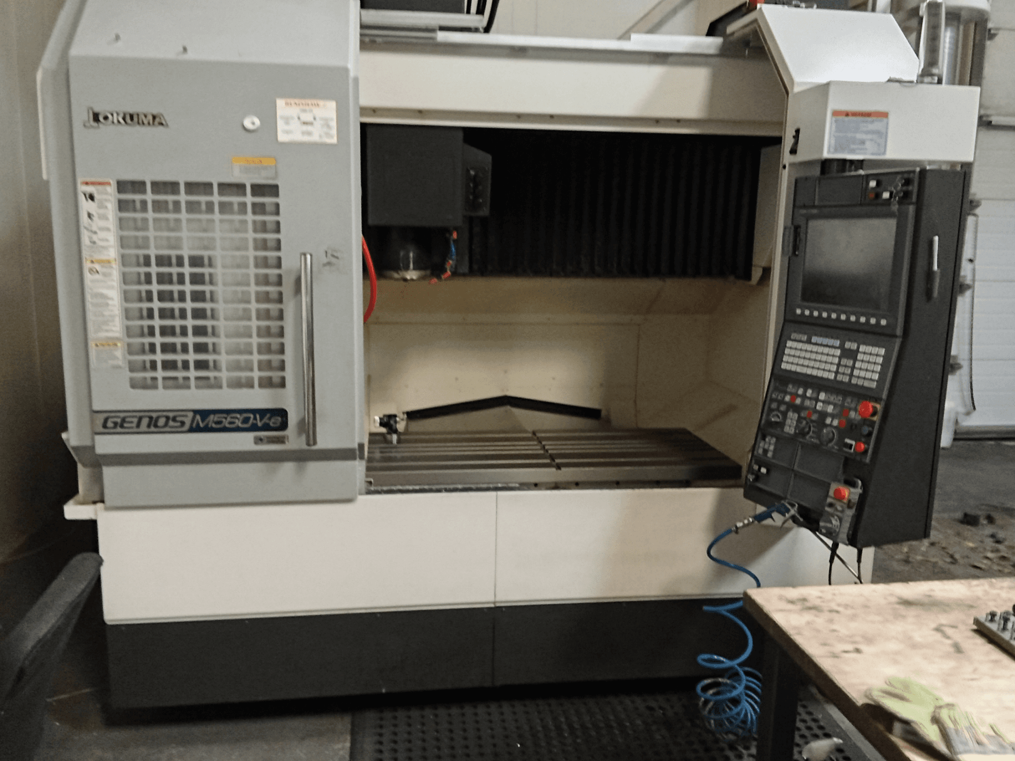 Okuma GENOS M560-V, egy függőleges megmunkálóközpont elülső nézete a vezérlőpanellel, a CNC-interfésszel és a látható vágási területtel.