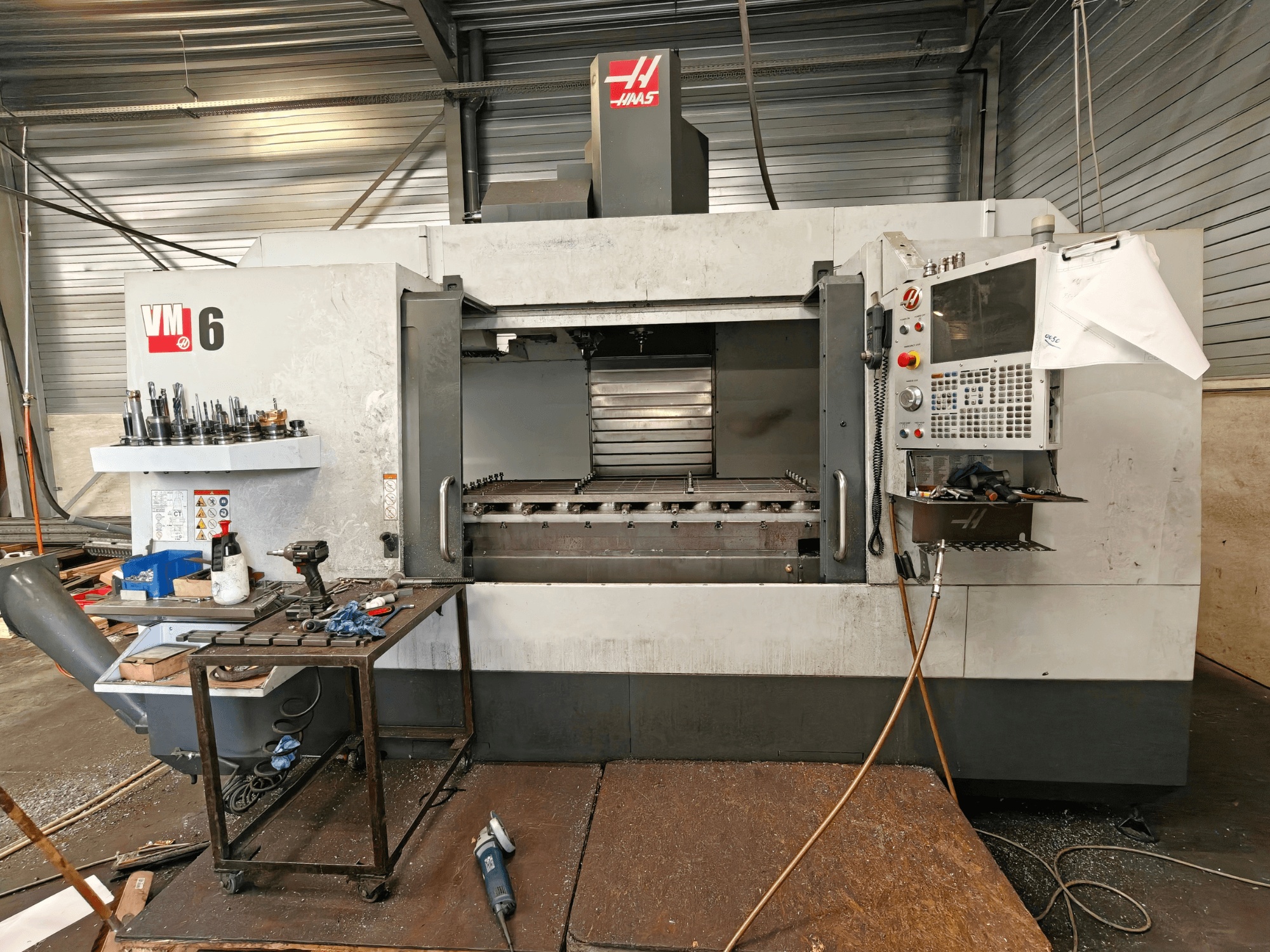 Haas VM-6 függőleges megmunkáló központ, elölnézet, látható a szerszámtároló, a vezérlőpanel és a munkaterületen lévő forgácsok.