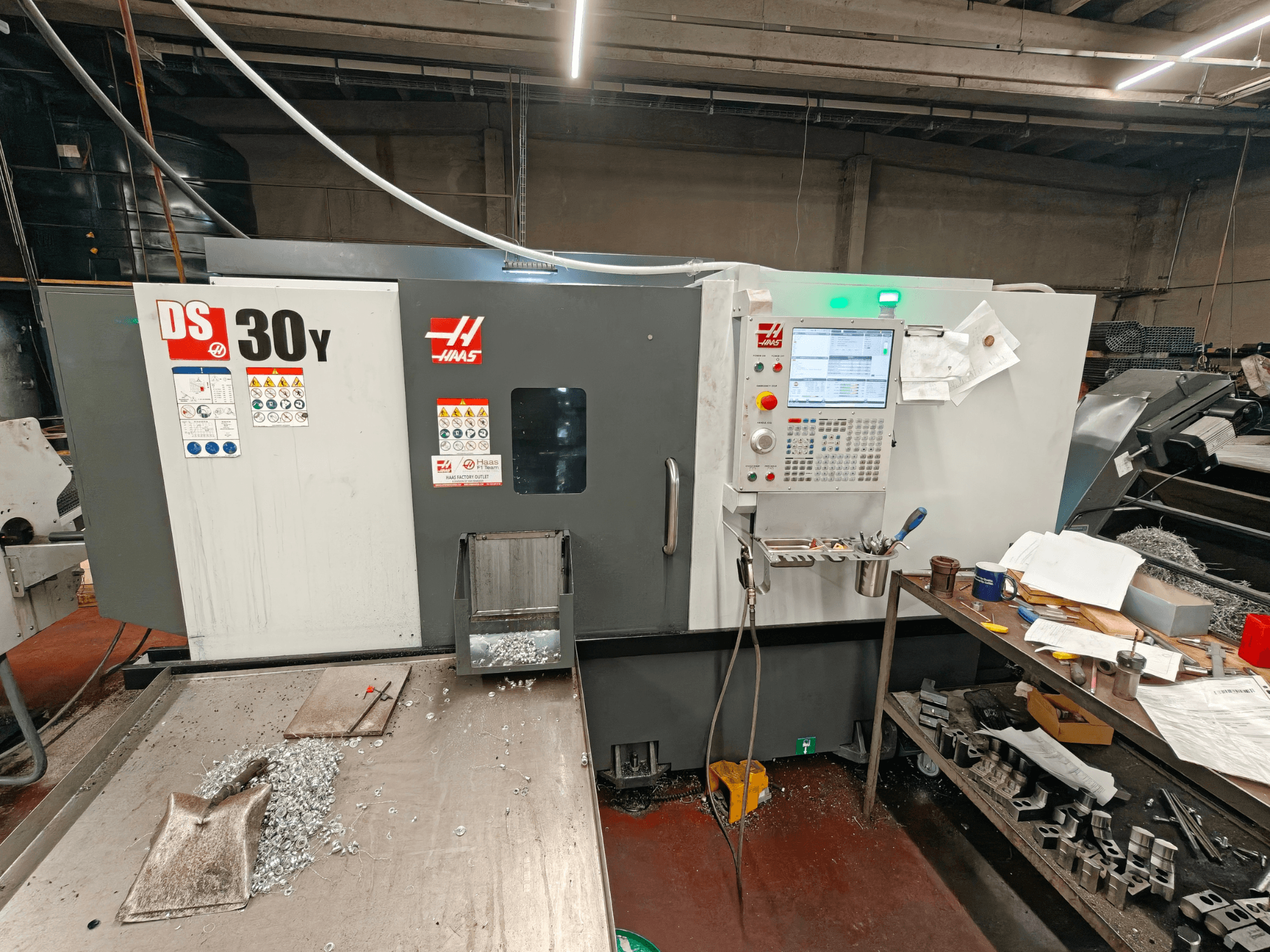 HAAS DS30Y vízszintes eszterga egy műhelyben, elölnézetből, amelyen látható a vezérlőpanel és a felületen heverő fémforgácsok.