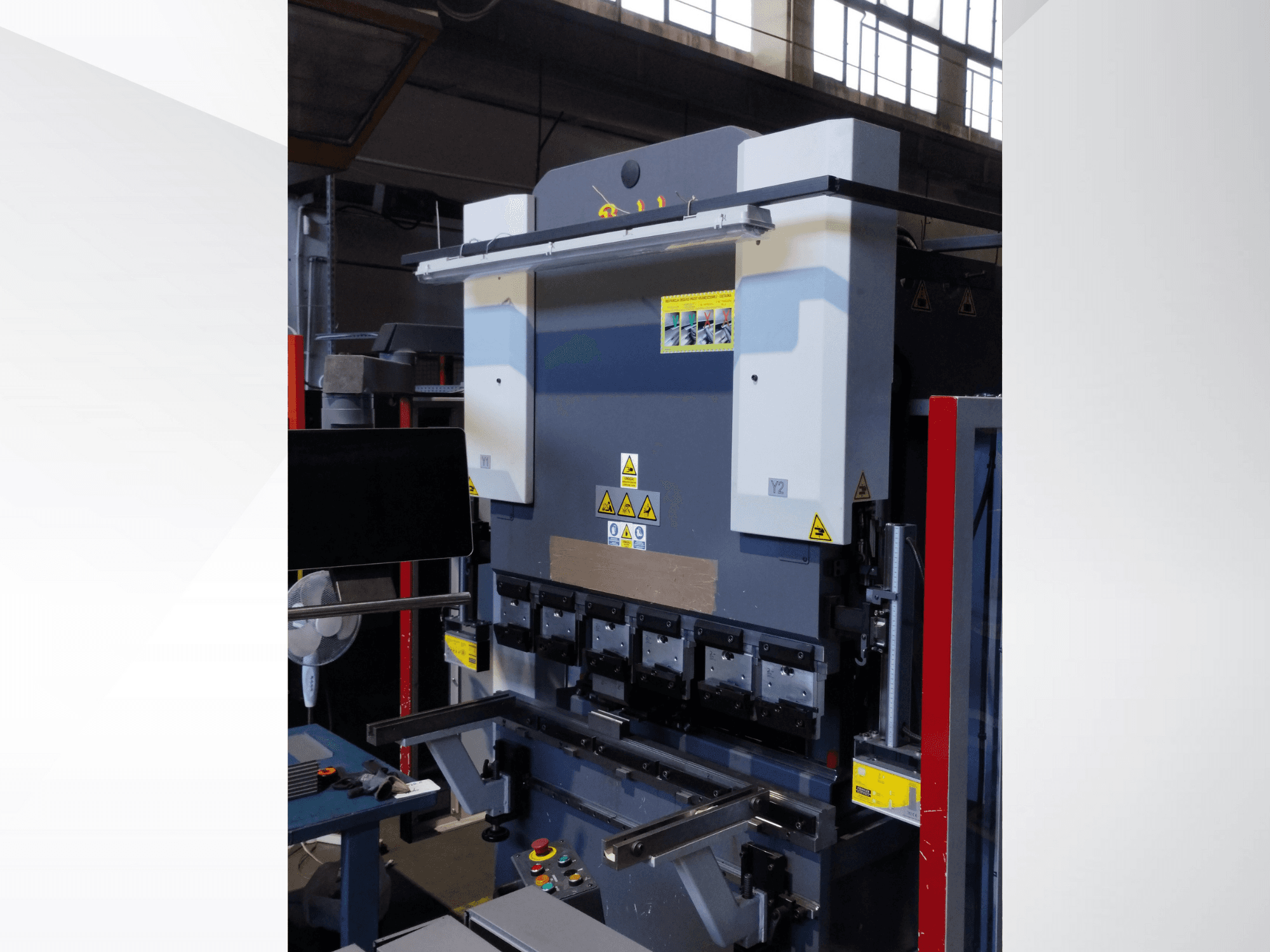 Sajtófékező gép, elölnézet. Látható kezelőszervekkel, biztonsági matricákkal és több szerszámtartóval rendelkezik a precíziós hajlításhoz.