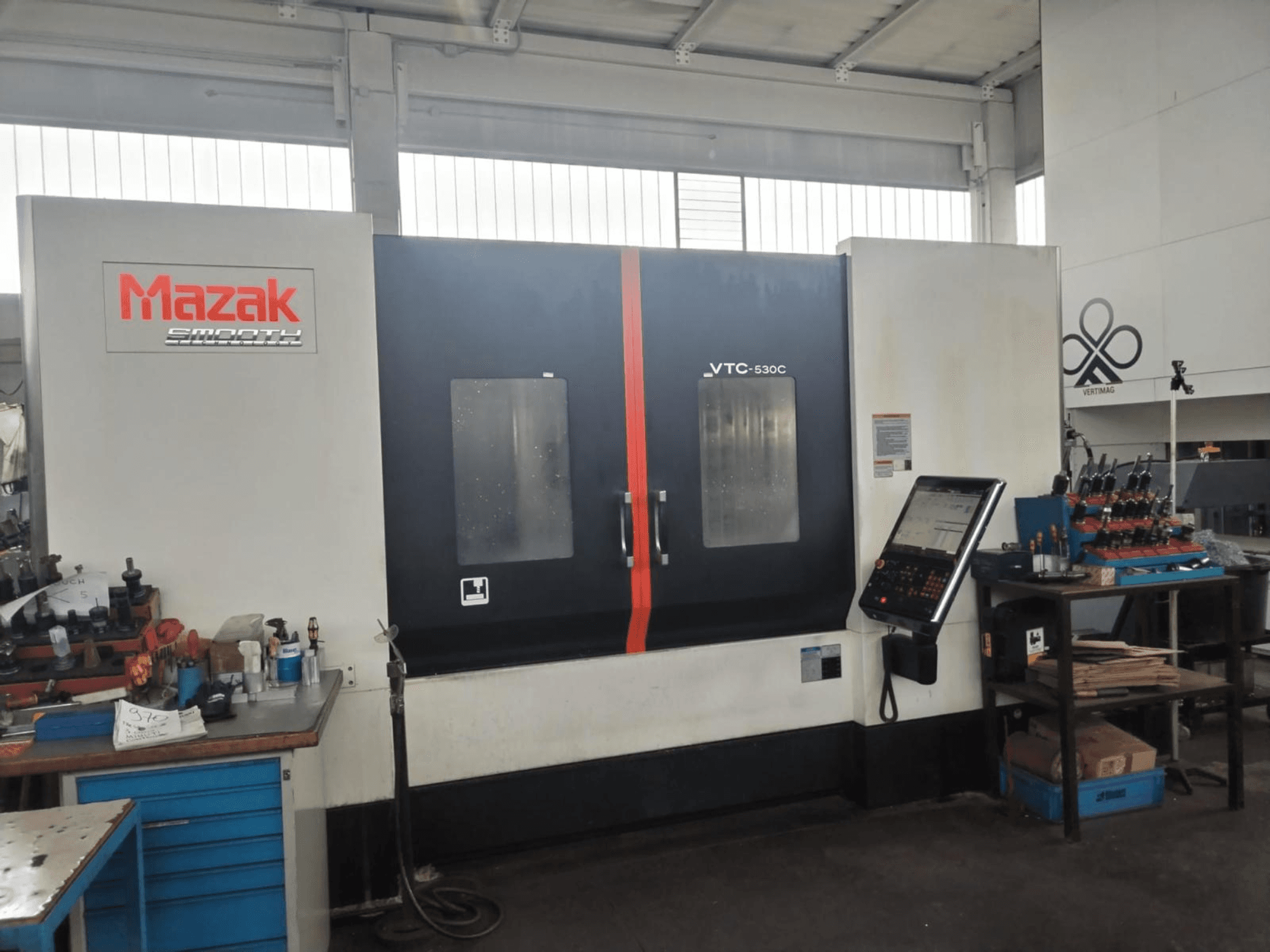 Mazak VTC-530C függőleges megmunkáló központ egy műhelyben, vezérlőpanellel és az oldalsó asztalon elhelyezett szerszámokkal.