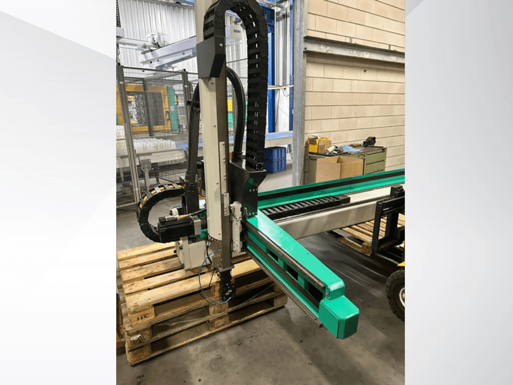 Arburg Multilift Select 15kg quer, a munkadarab-kezelő rendszer oldalnézetben, fa raklapokon, a robotkar és a vezérlőelemek bemutatása.
