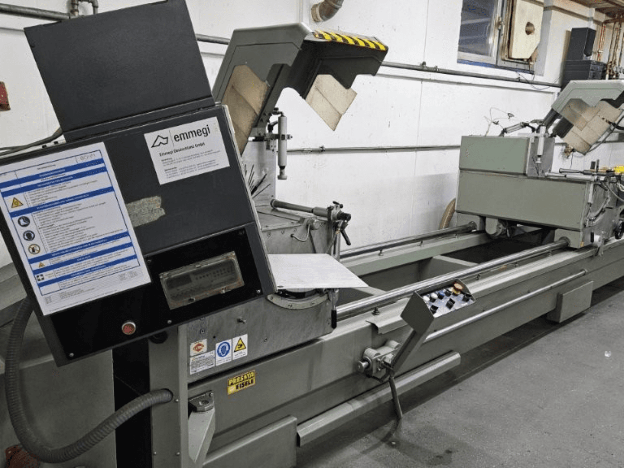 Emmegi ipari vágógép, előlnézet, vezérlőpanel, biztonsági címkék és működési elemek.