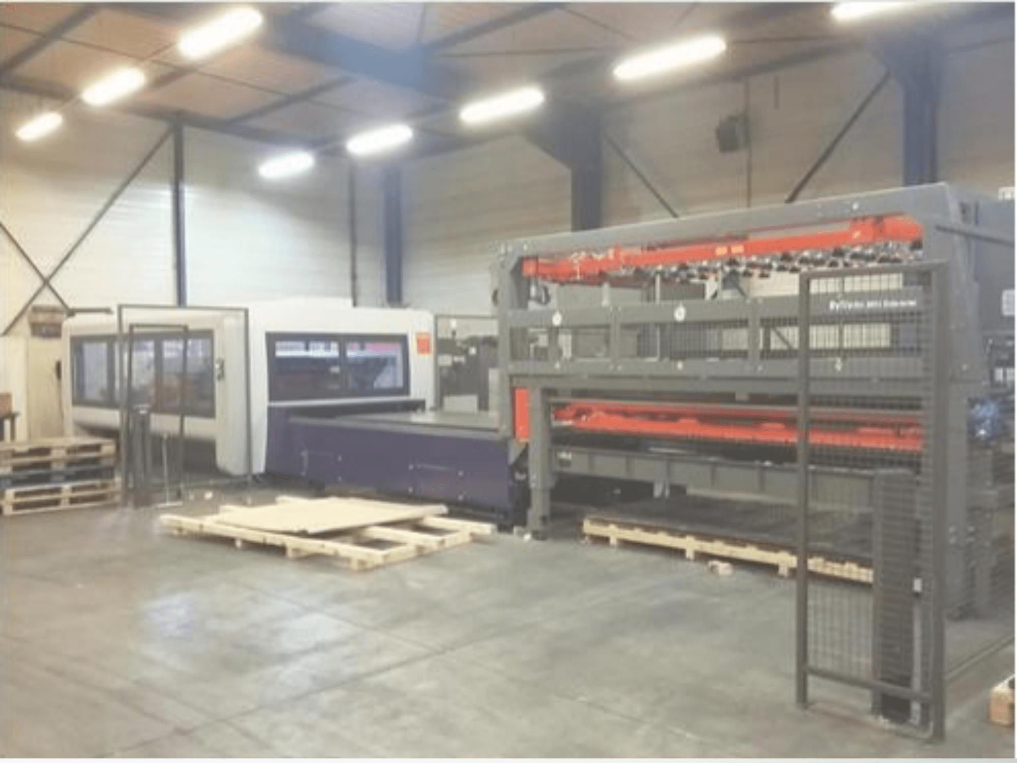 Ipari gépek beállítása egy raktárban; egy szürke lézervágó és egy lila CNC-router, elölnézetben raklapokkal.